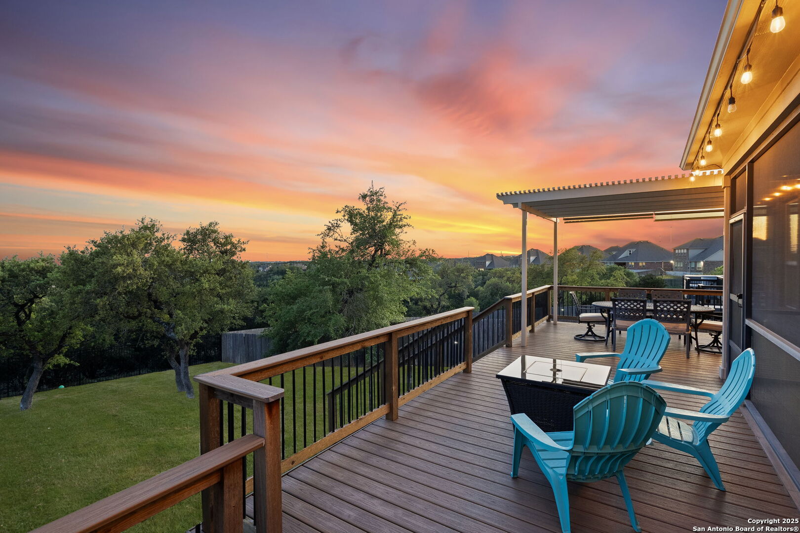Wooden deck with turquoise chairs and covered dining area overlooking trees at sunset.