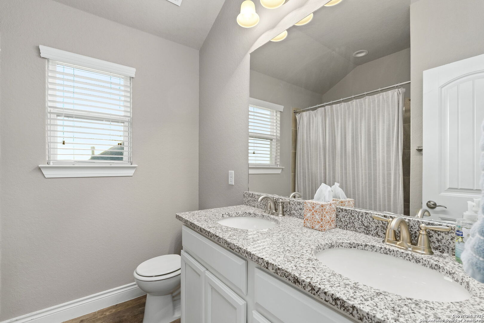 Bathroom with a double-sink granite vanity, large mirror, window, and curtained shower.