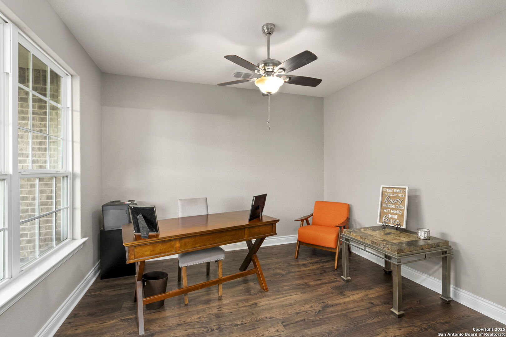 Home office with a wooden desk, orange armchair, large windows, and dark wood floors.