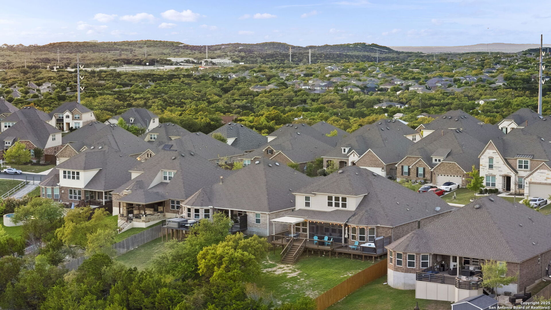 Aerial view of a suburban neighborhood, with homes in the foreground and wooded hills beyond.