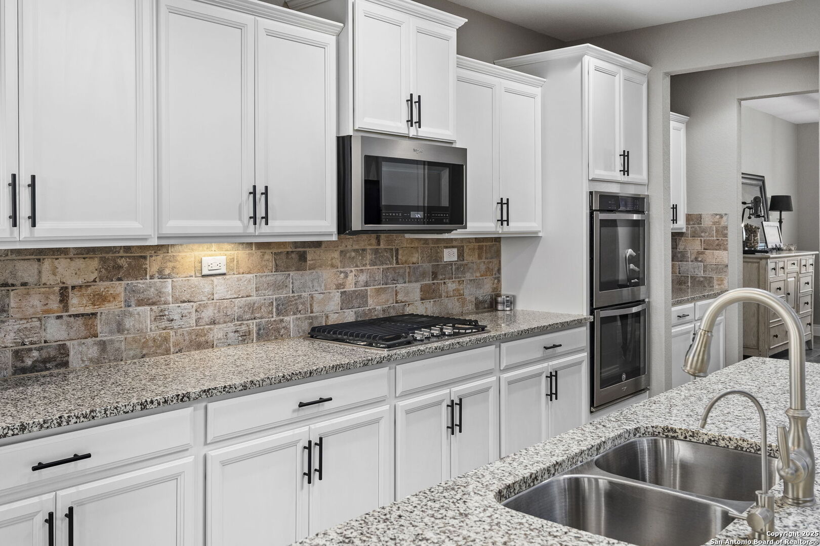 Kitchen with white cabinets, granite counters, stone-tile backsplash, stainless appliances, and a double-basin sink.