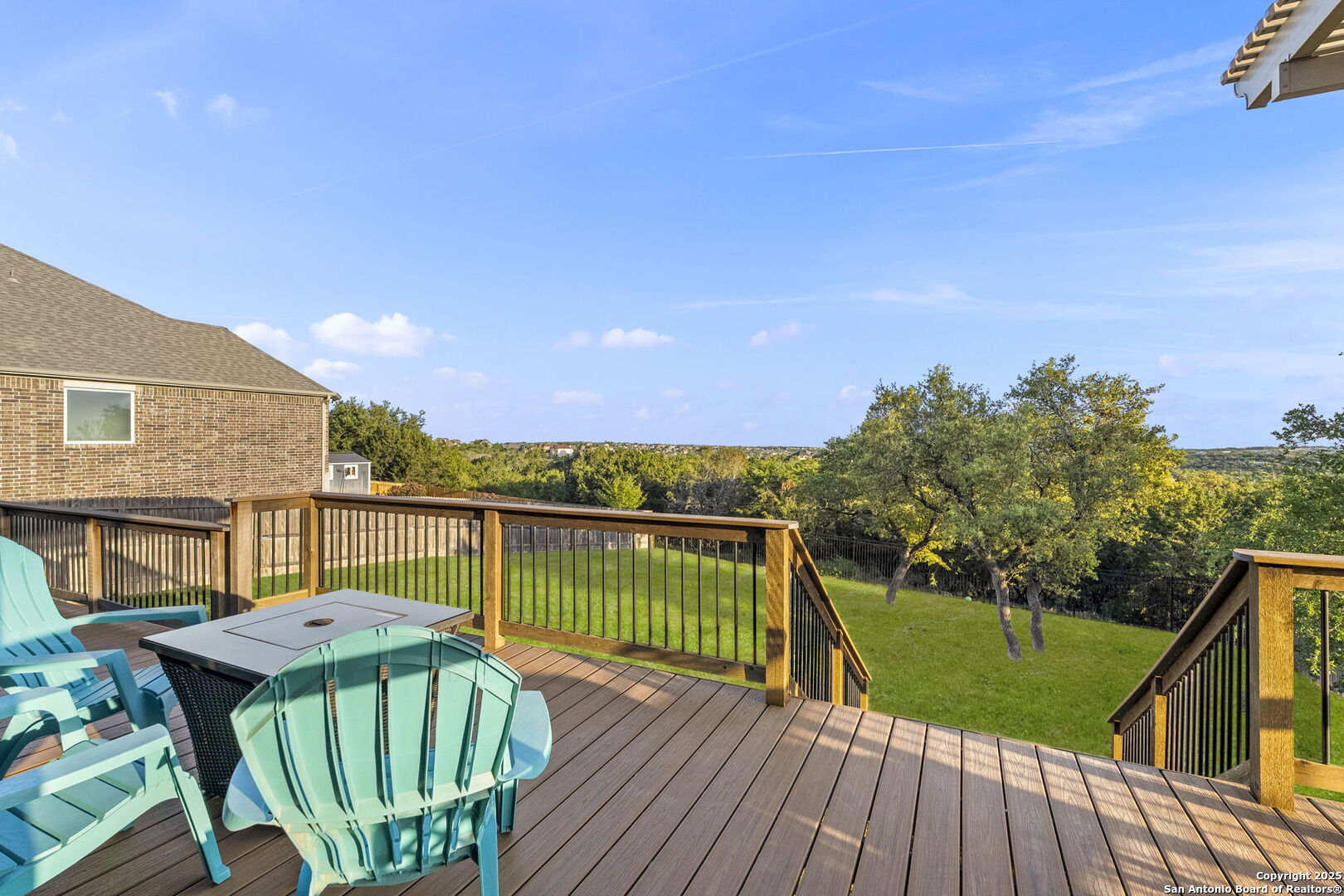 Wooden deck with turquoise chairs and fire table overlooking a fenced, tree-lined backyard.