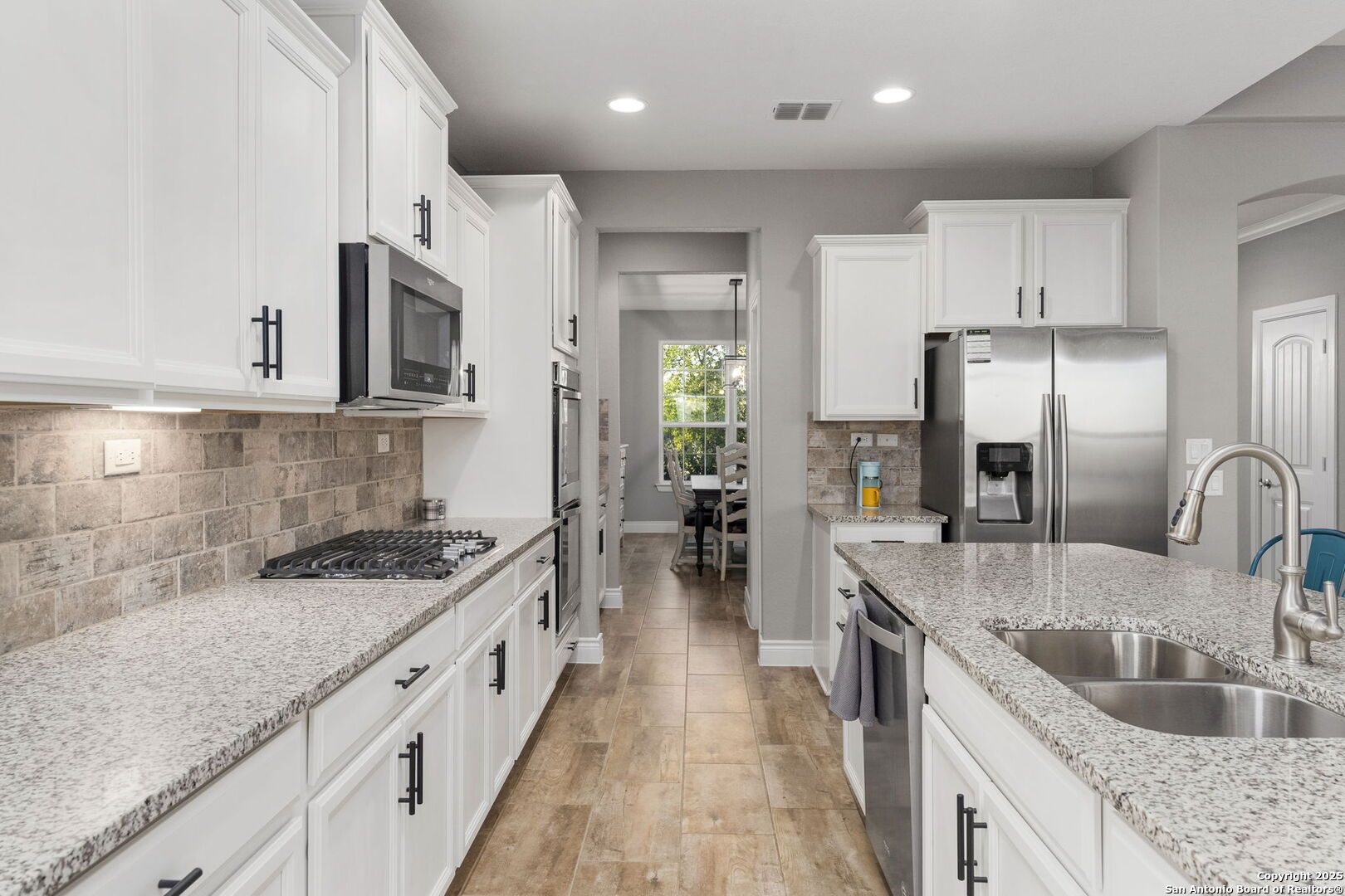 Kitchen with white cabinets, granite counters, stainless steel appliances, and a large island with a double sink.