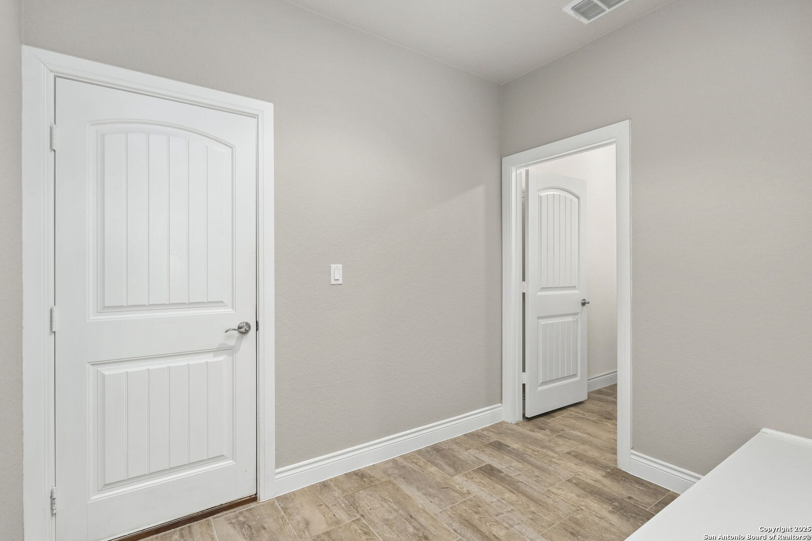 Unfurnished passage with wood-look tile flooring and two white paneled doors.