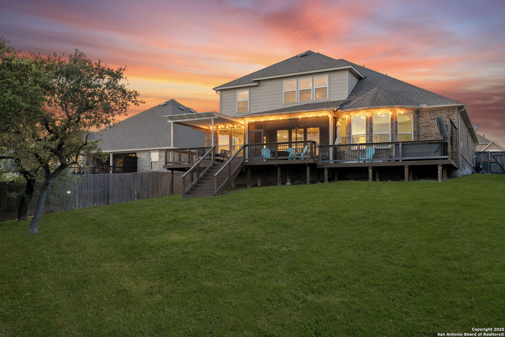 Two-story home with an illuminated raised deck and lawn beneath a colorful sunset.