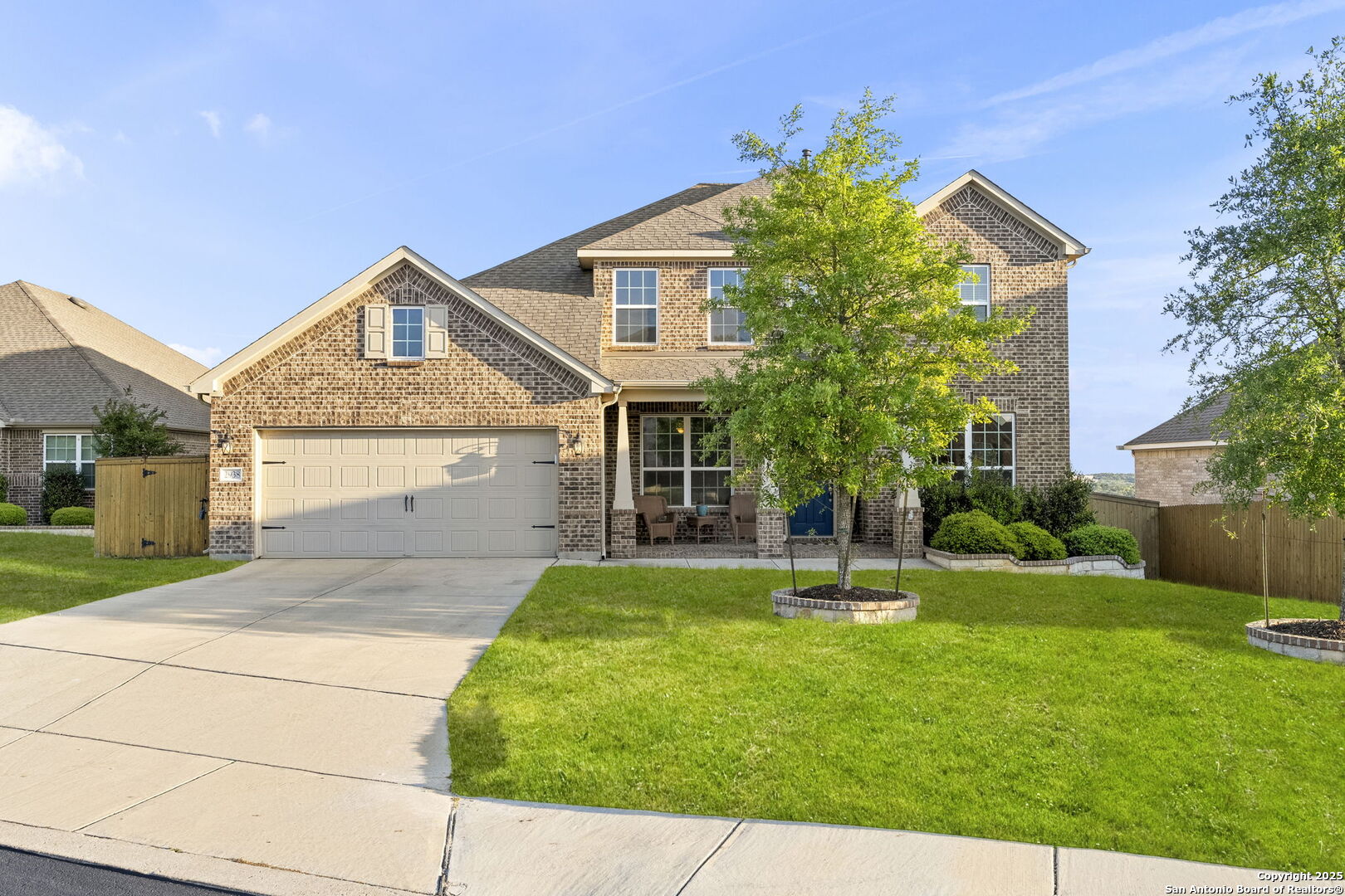 Two-story brick home with a two-car garage, covered porch, and broad green lawn.