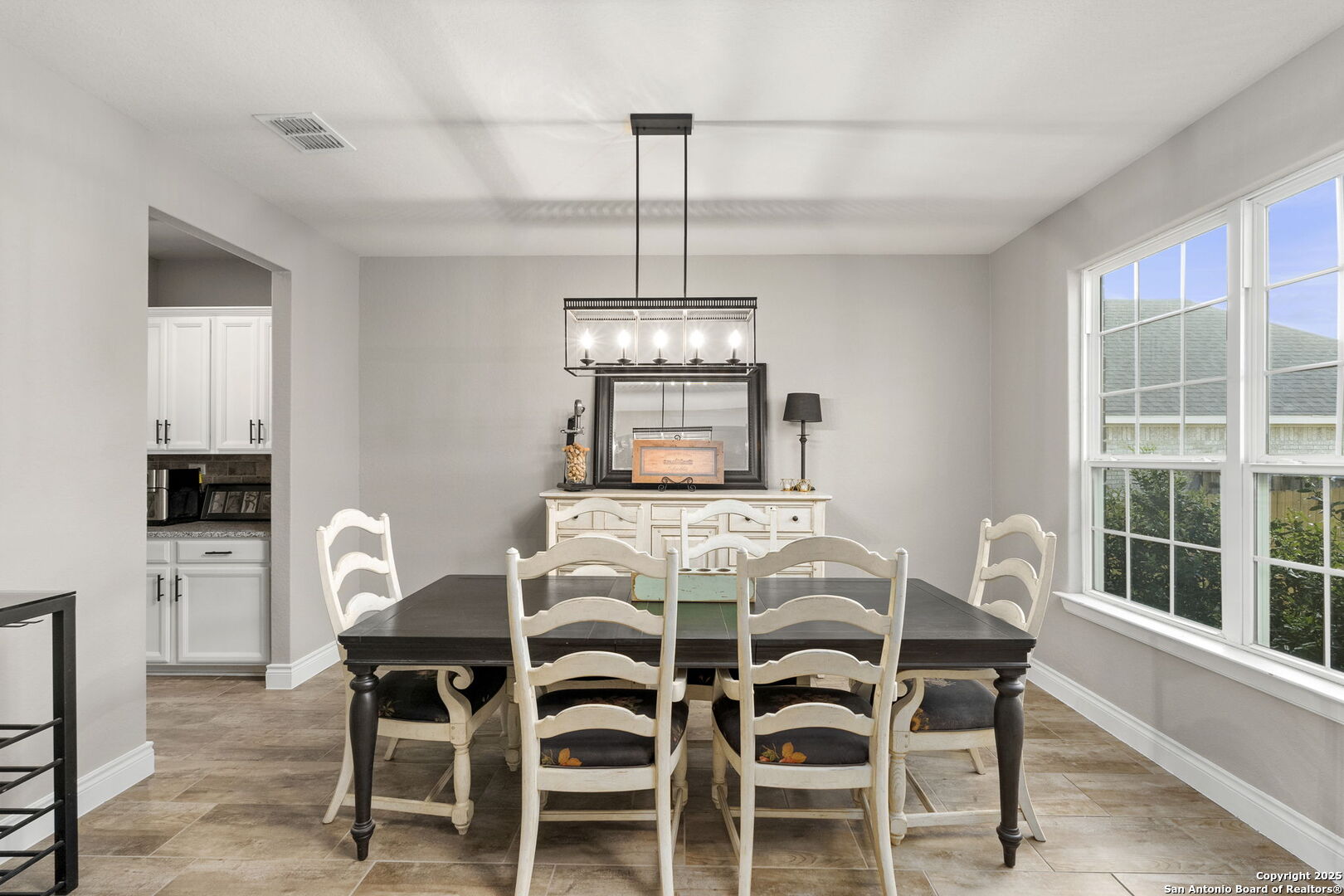 Dining room with a dark table, white chairs, chandelier, and large windows.