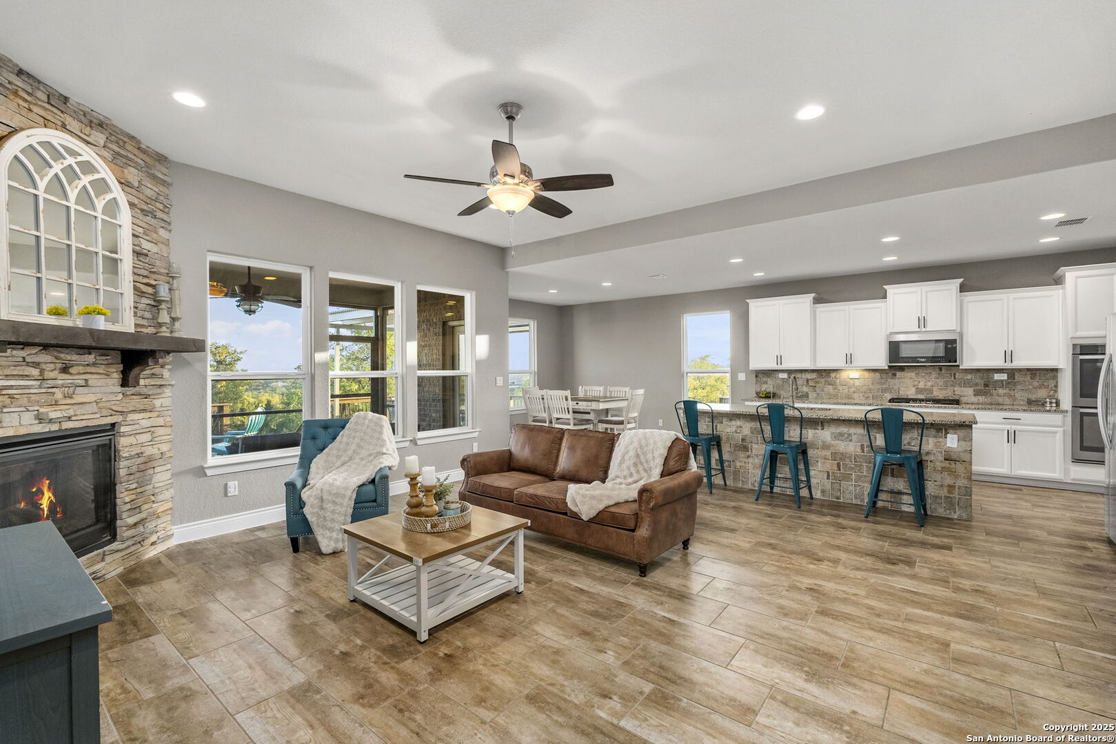 Open-plan living room and kitchen with a stone fireplace, brown sofa, and white cabinets.