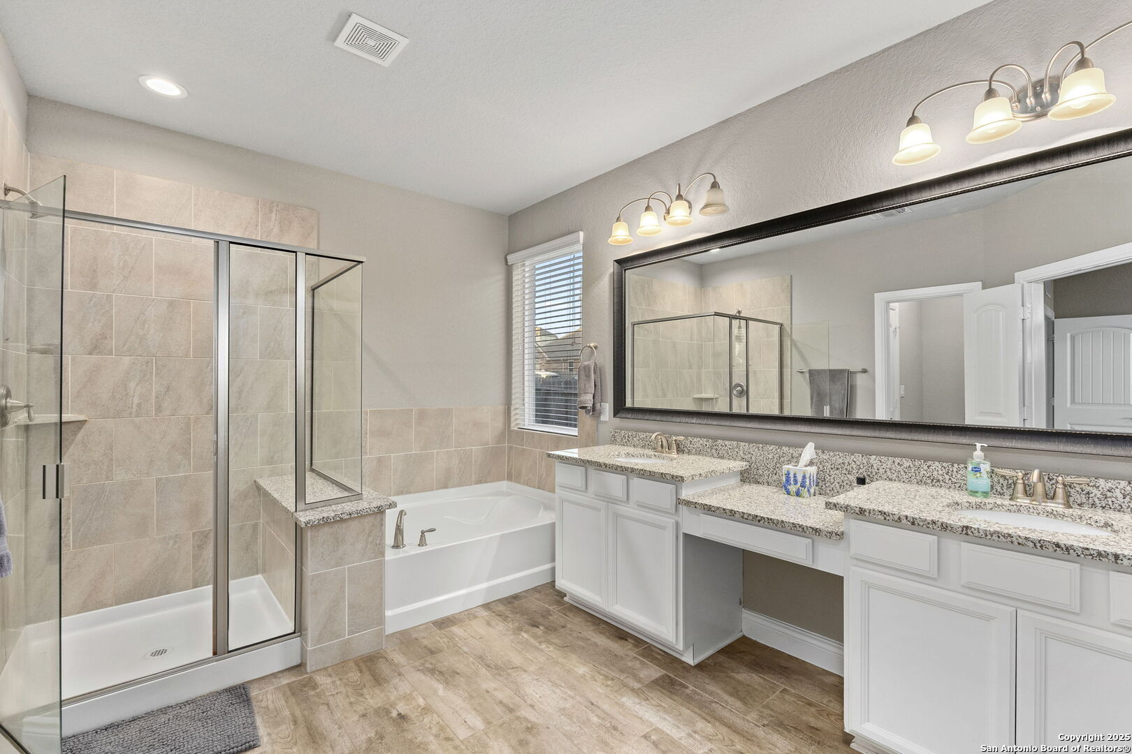 Bathroom with a glass shower, separate soaking tub, and long double vanity beneath a large mirror.