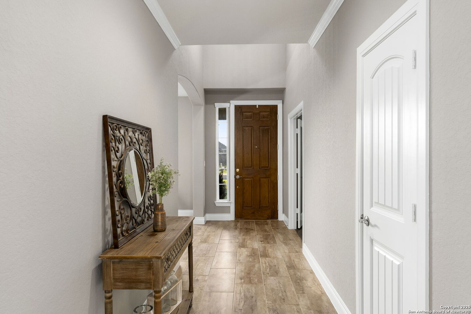 Entry hall with tan tile floors, a dark wood front door, and a console table with a decorative mirror.