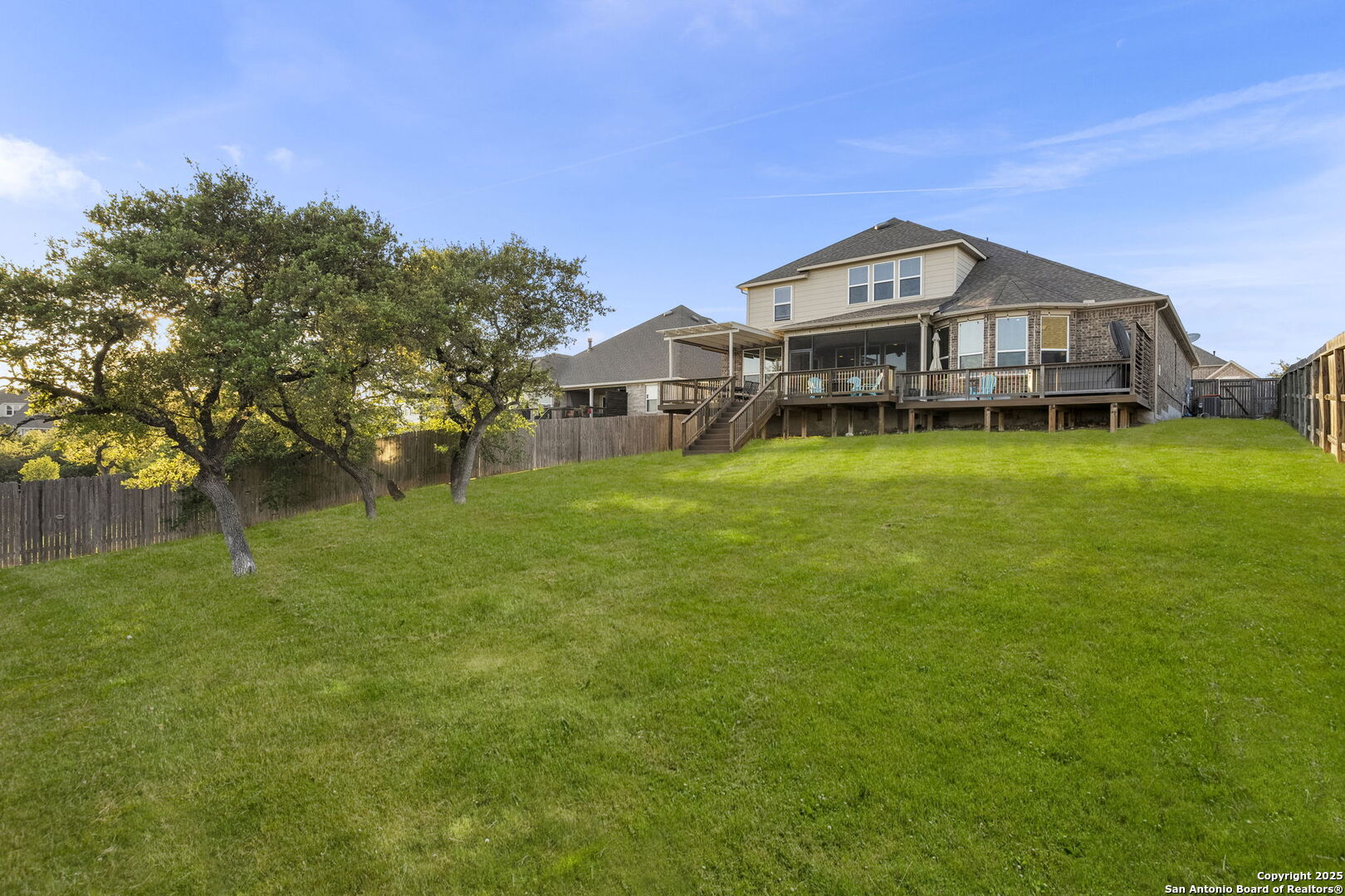 Two-story home with a raised deck overlooking a broad lawn and mature trees.