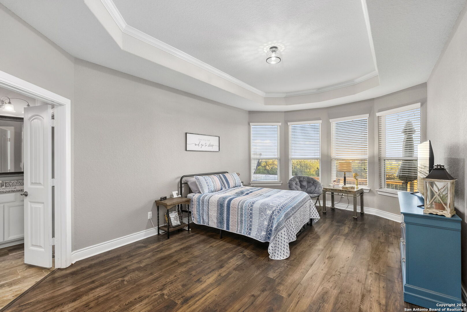 Bedroom with blue-and-white bedding, a tray ceiling, and four windows with blinds.