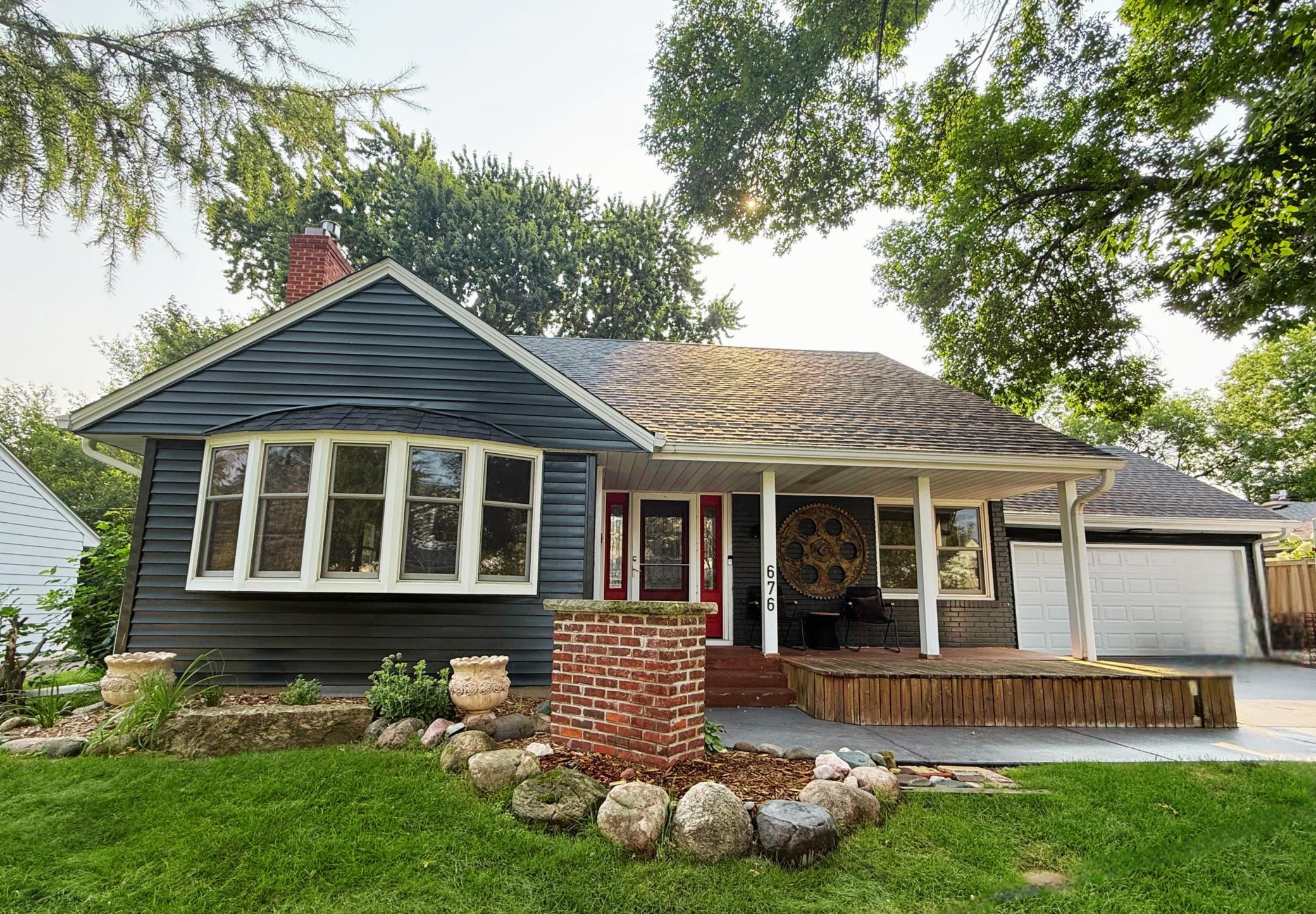 Dark blue-gray house with a red front door, covered porch, attached garage, and rock garden.