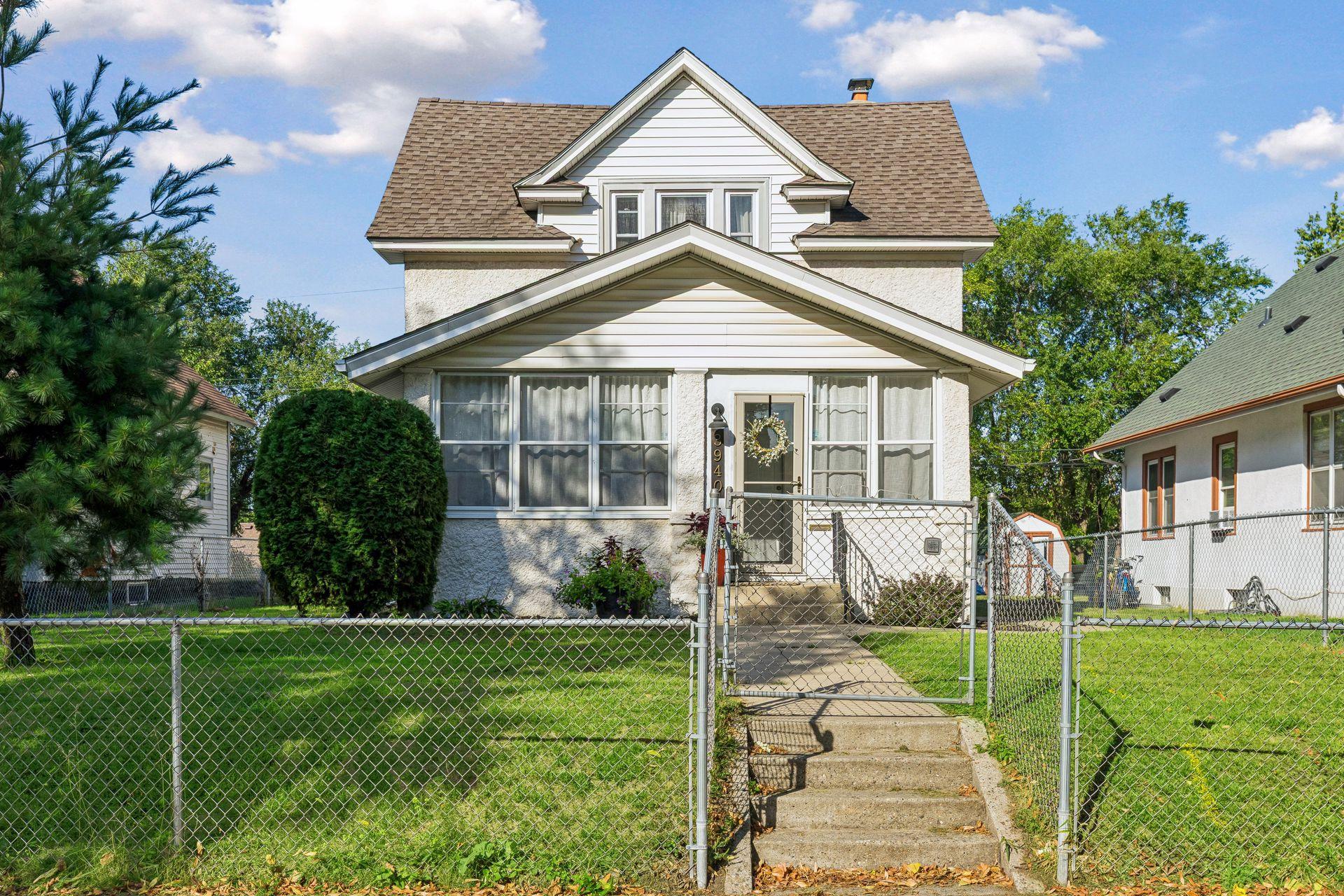 White two-story house with a covered porch, chain-link fence, and walkway to the front door.