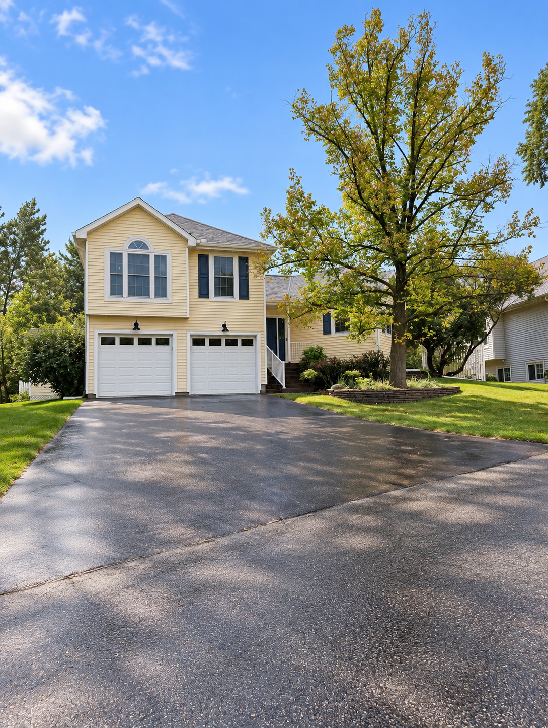 Pale yellow two-story house with a double garage and large autumn tree beside the driveway.