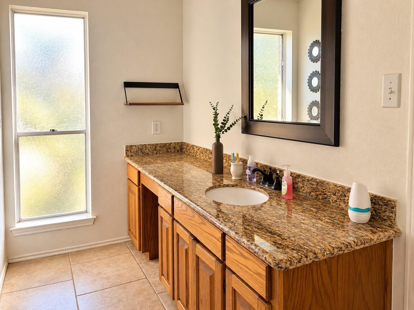 Bathroom vanity with a mottled granite counter, warm wood cabinets, and a large dark-framed mirror.