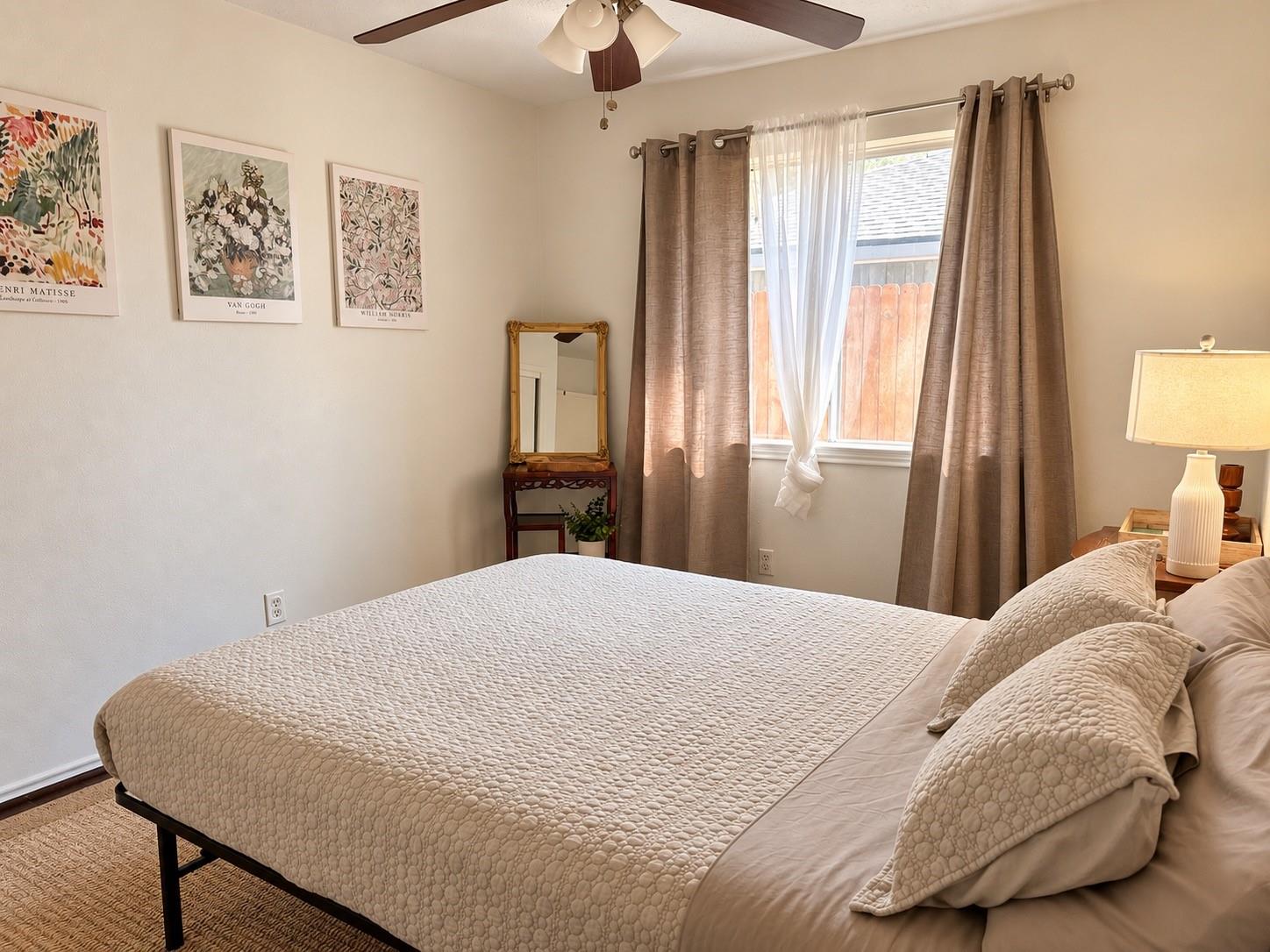 Furnished bedroom with a cream quilted bed, taupe curtains, and framed art prints.