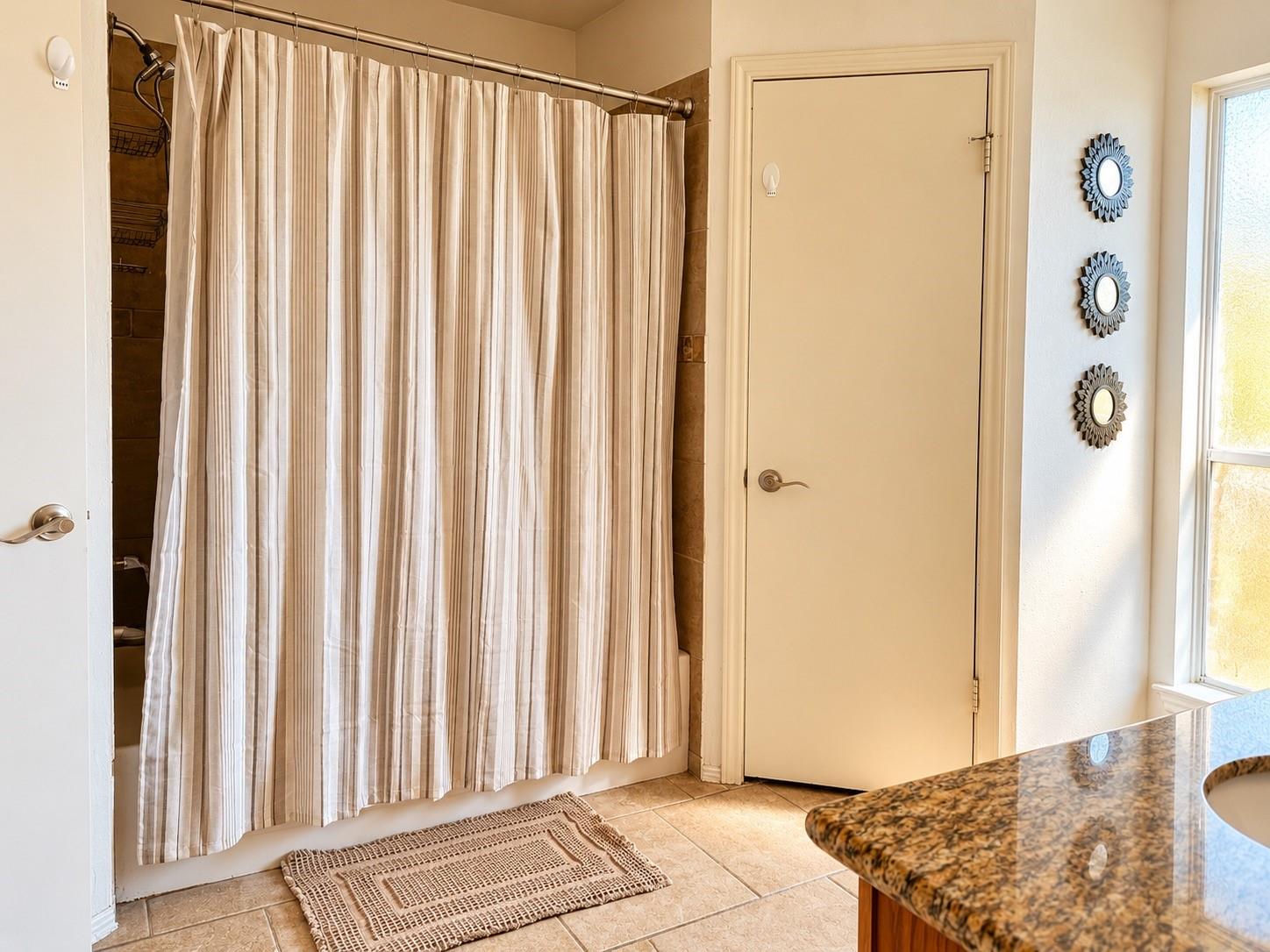 Bathroom with striped shower curtain, tiled floor, and granite vanity beside a window.