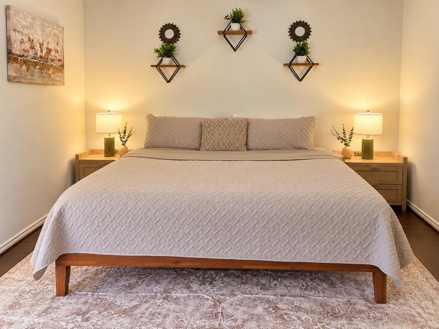 Staged bedroom with a large pale-quilted bed, matching wooden nightstands, and warm bedside lamps.