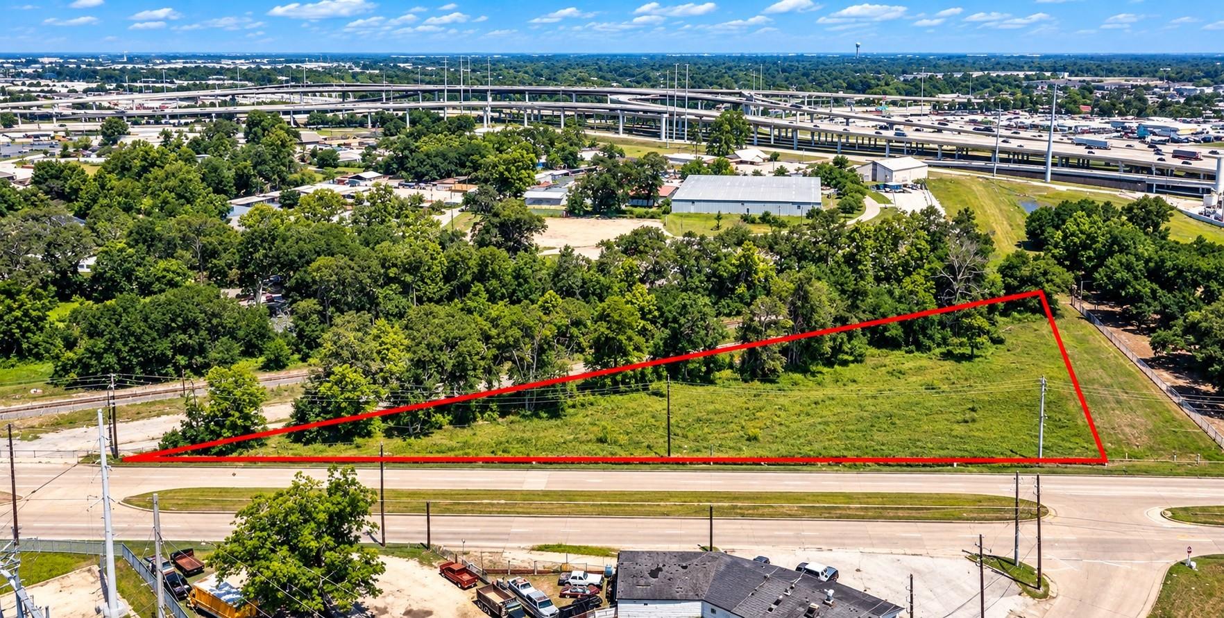 Aerial view of a grassy vacant lot outlined in red beside a wide road and highway interchange.