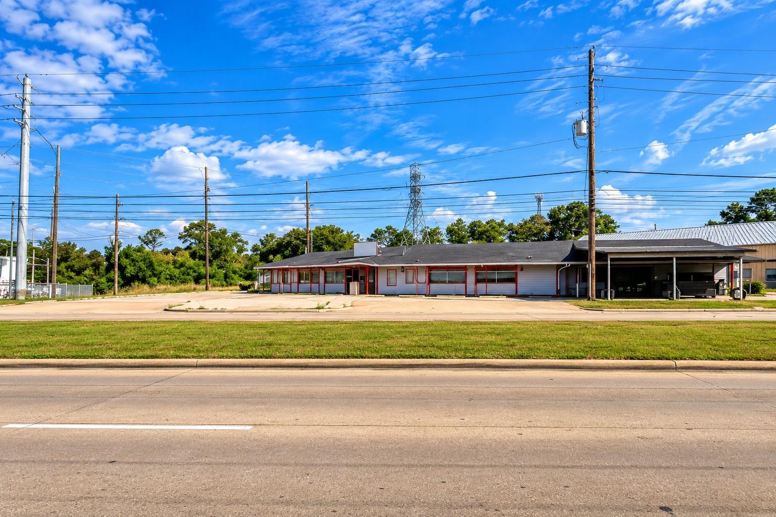 Single-story commercial building with red trim and a covered open bay beside a roadside lot.