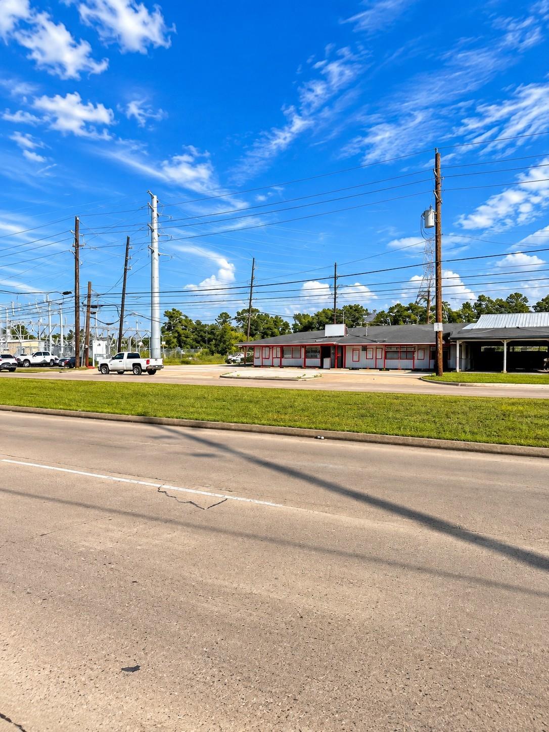 Single-story commercial building with red trim and covered parking beside a broad road.