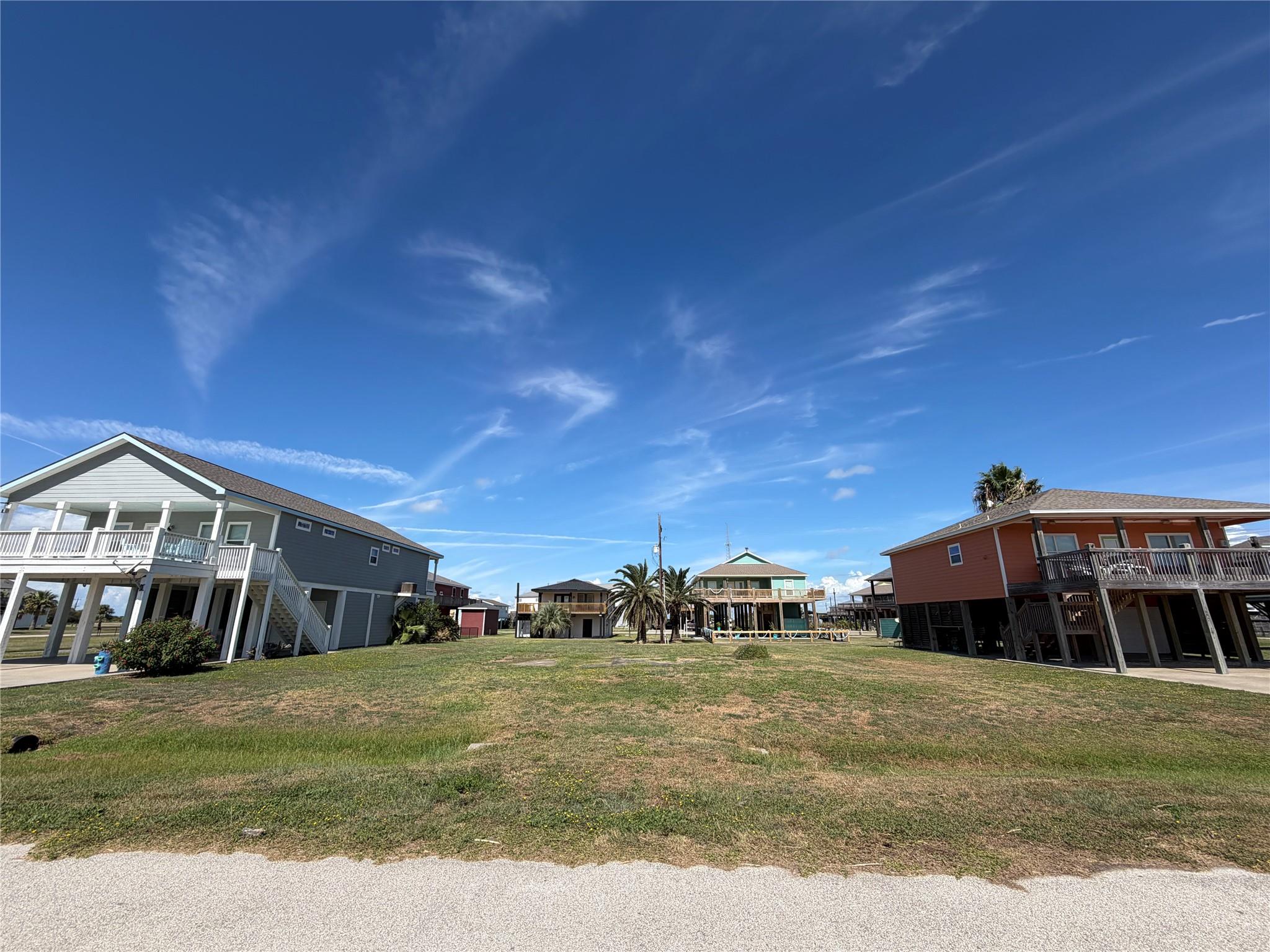 Elevated coastal homes with broad decks surrounding a grassy open lot.