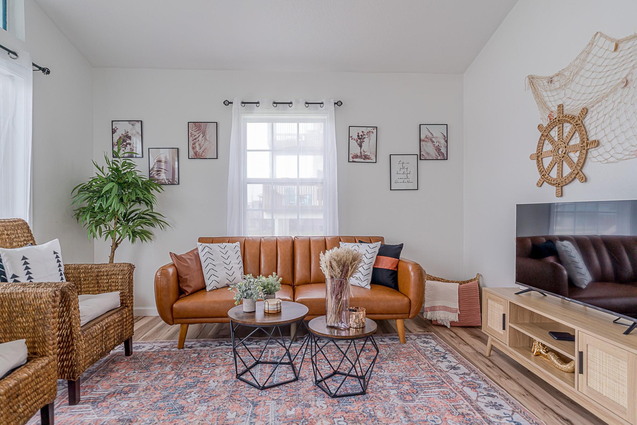 Staged living room with a brown leather sofa, wicker chairs, and a large patterned rug.