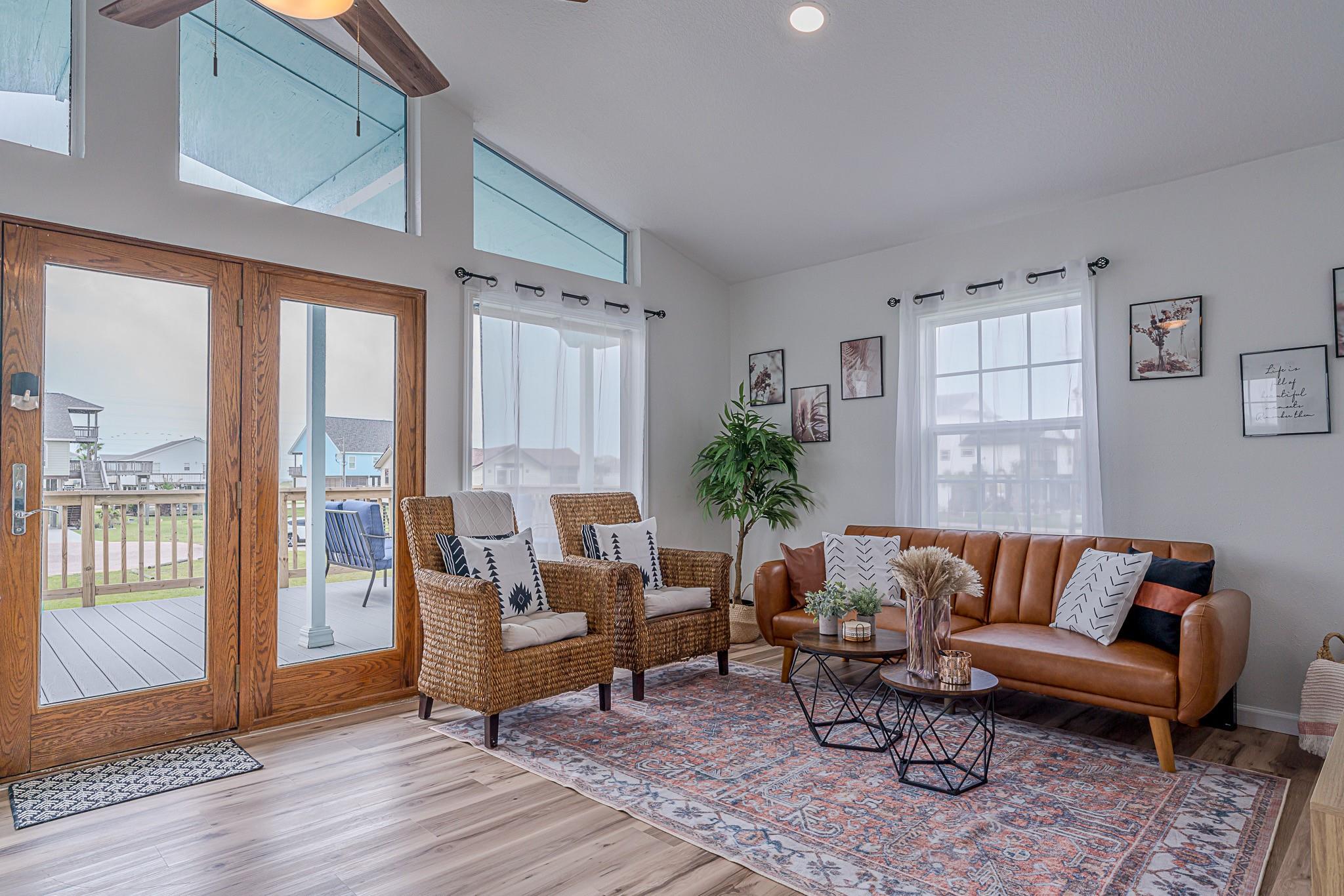 Living room with a brown leather sofa, woven armchairs, and wood-framed glass doors opening to a deck.