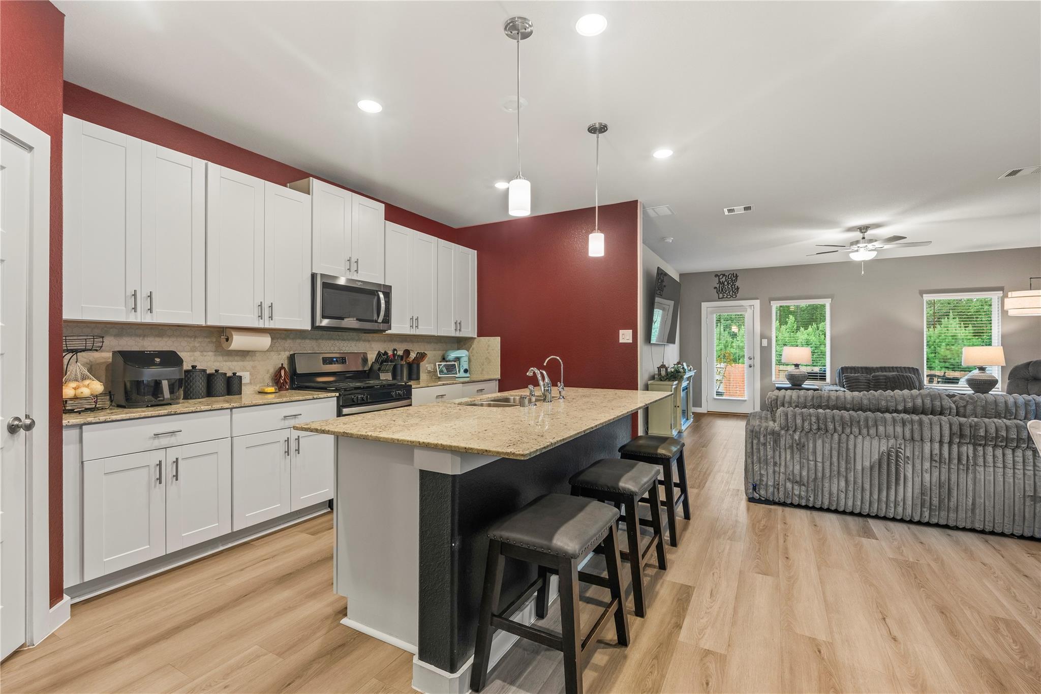 Kitchen with a large granite island and bar seating, opening into a living room with gray sofas.