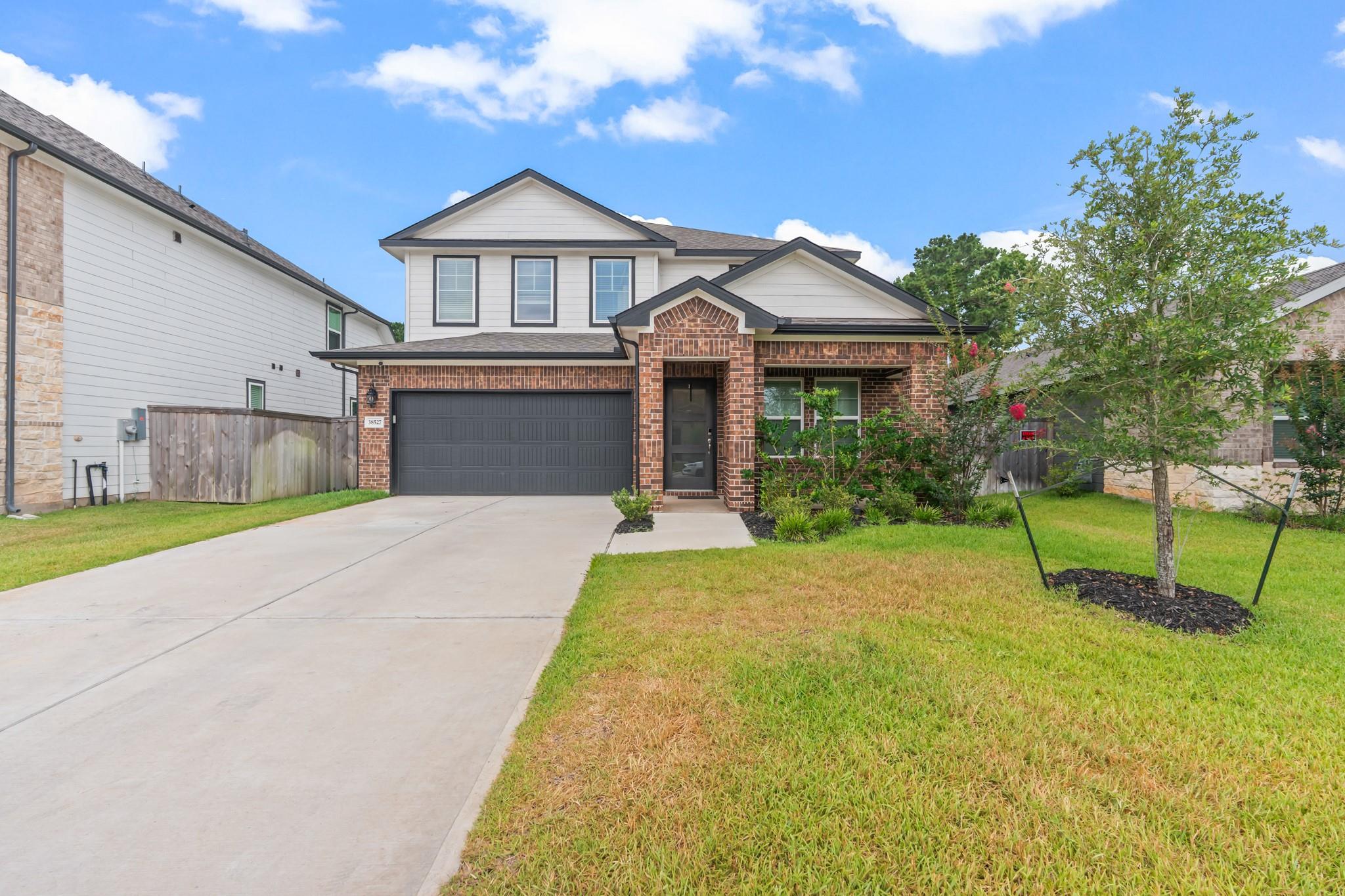 Two-story brick-and-siding home with a double garage, wide driveway, and front lawn.