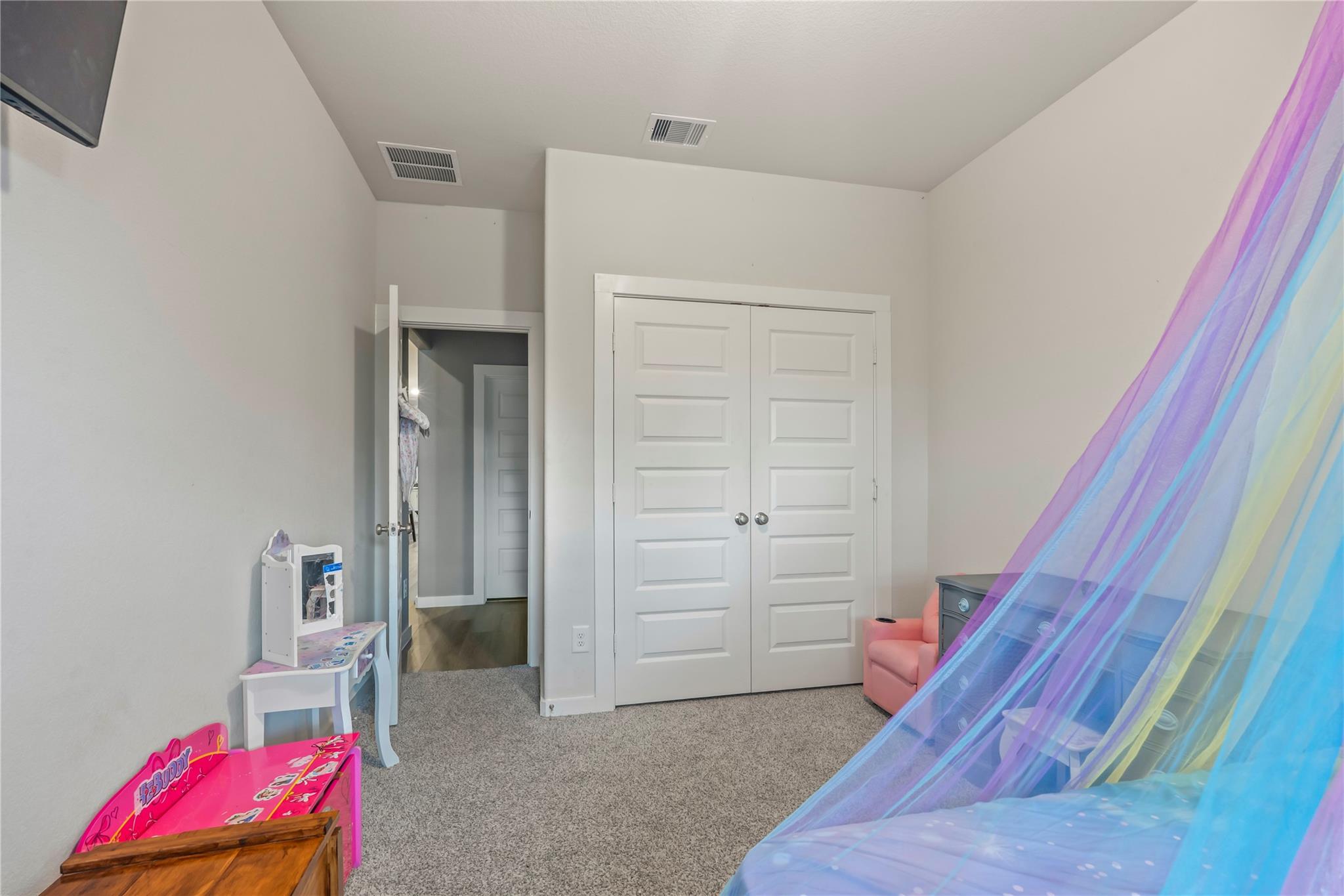 Child’s bedroom with a colorful bed canopy, pink play table, and white double closet doors.