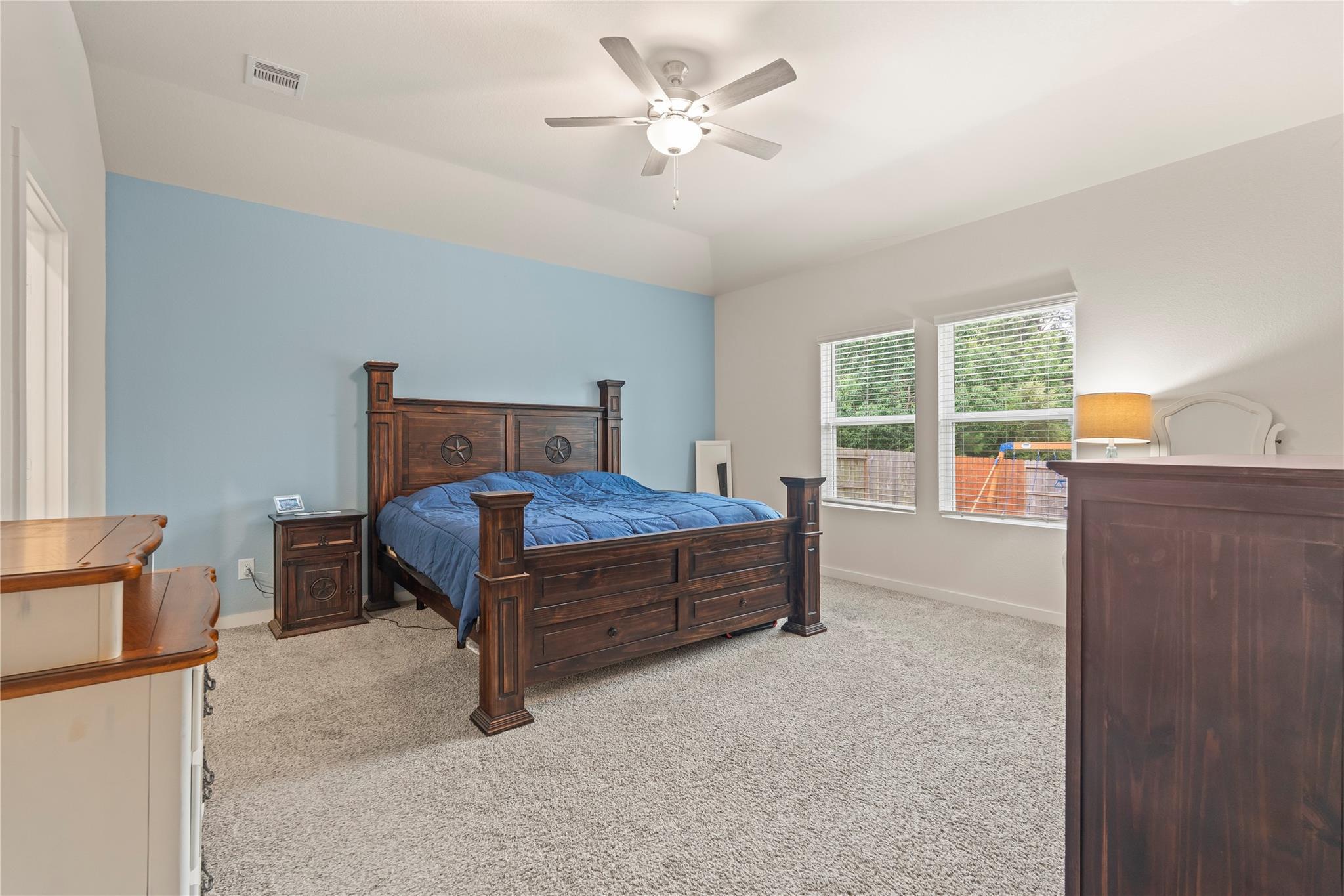 Furnished bedroom with a dark wood bed, blue accent wall, carpet, and two windows.