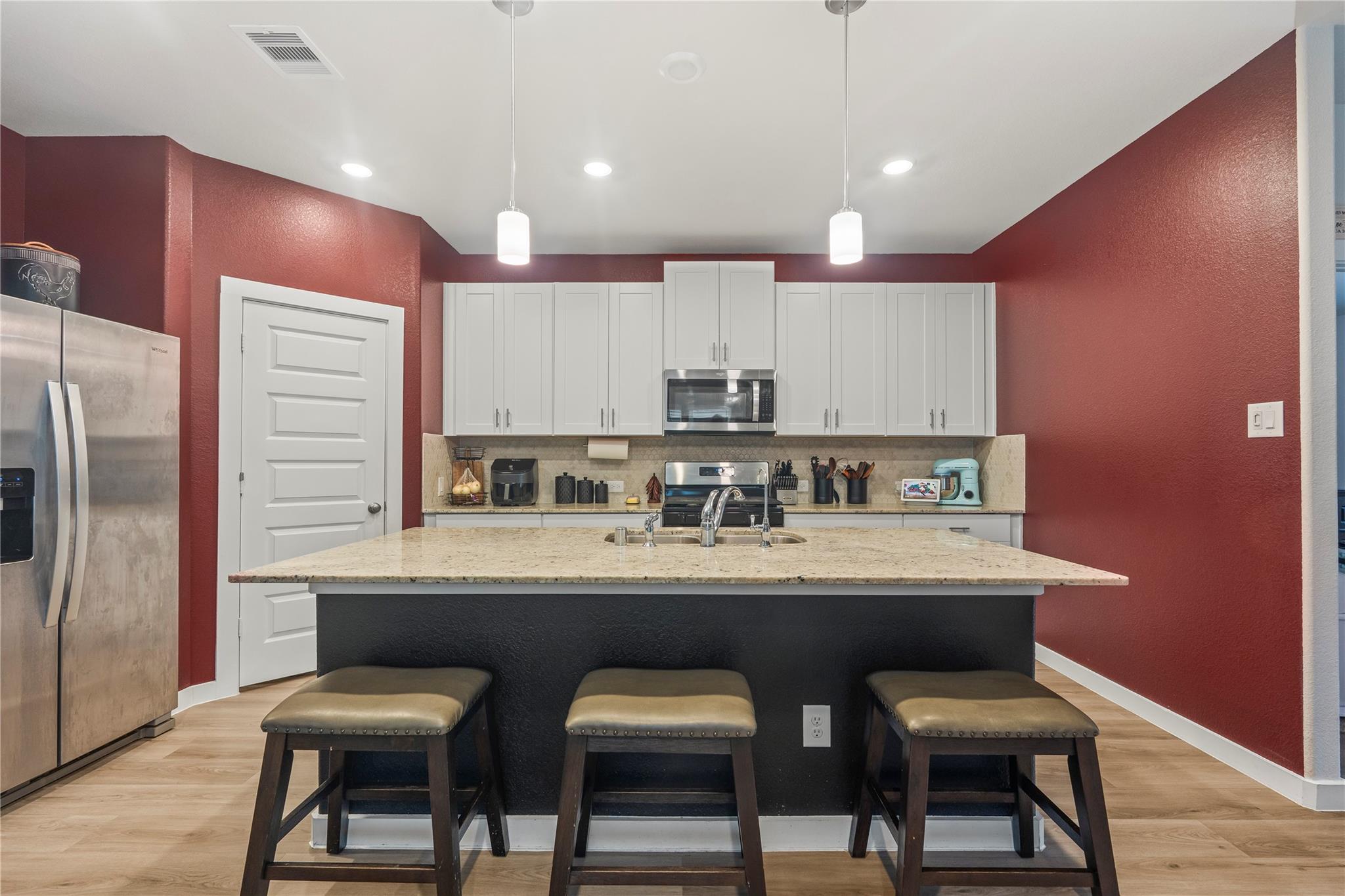Kitchen with a granite-topped island, three stools, white cabinets, and deep red walls.