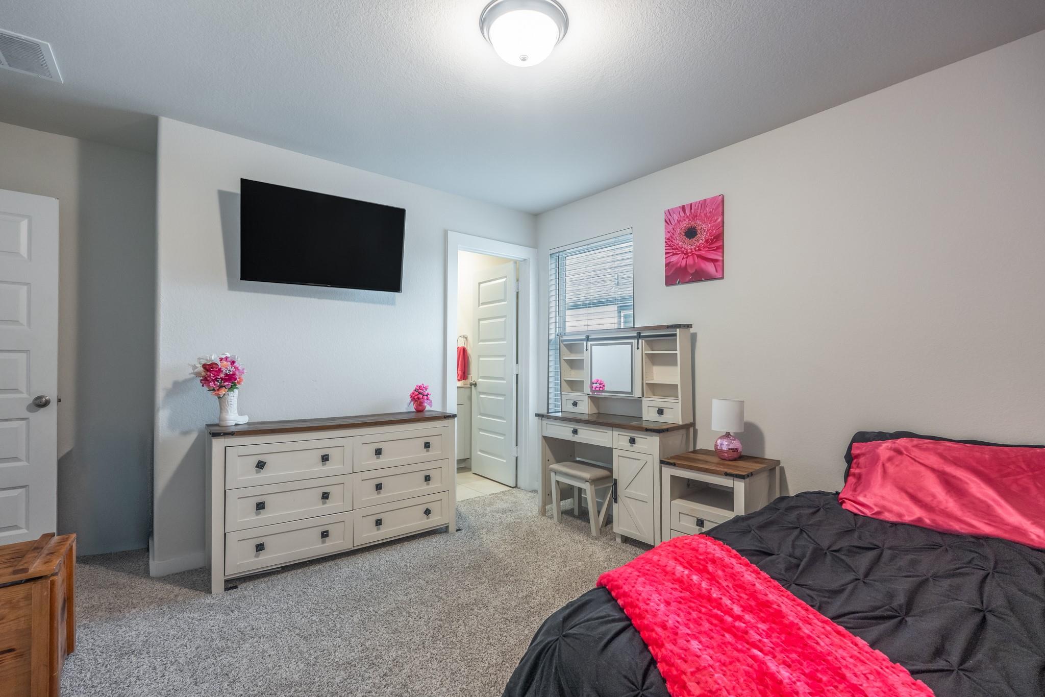 Furnished bedroom with a black bedspread, bright pink accents, dresser, and vanity desk.