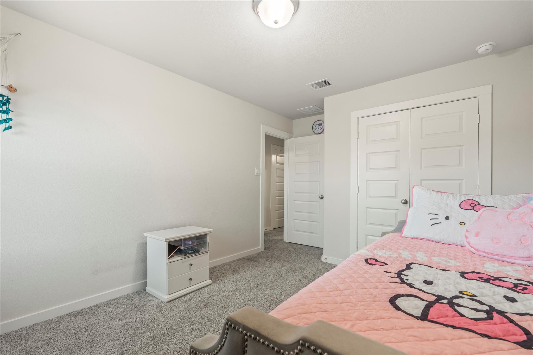 Bedroom with pink Hello Kitty bedding, gray carpet, and white closet doors.