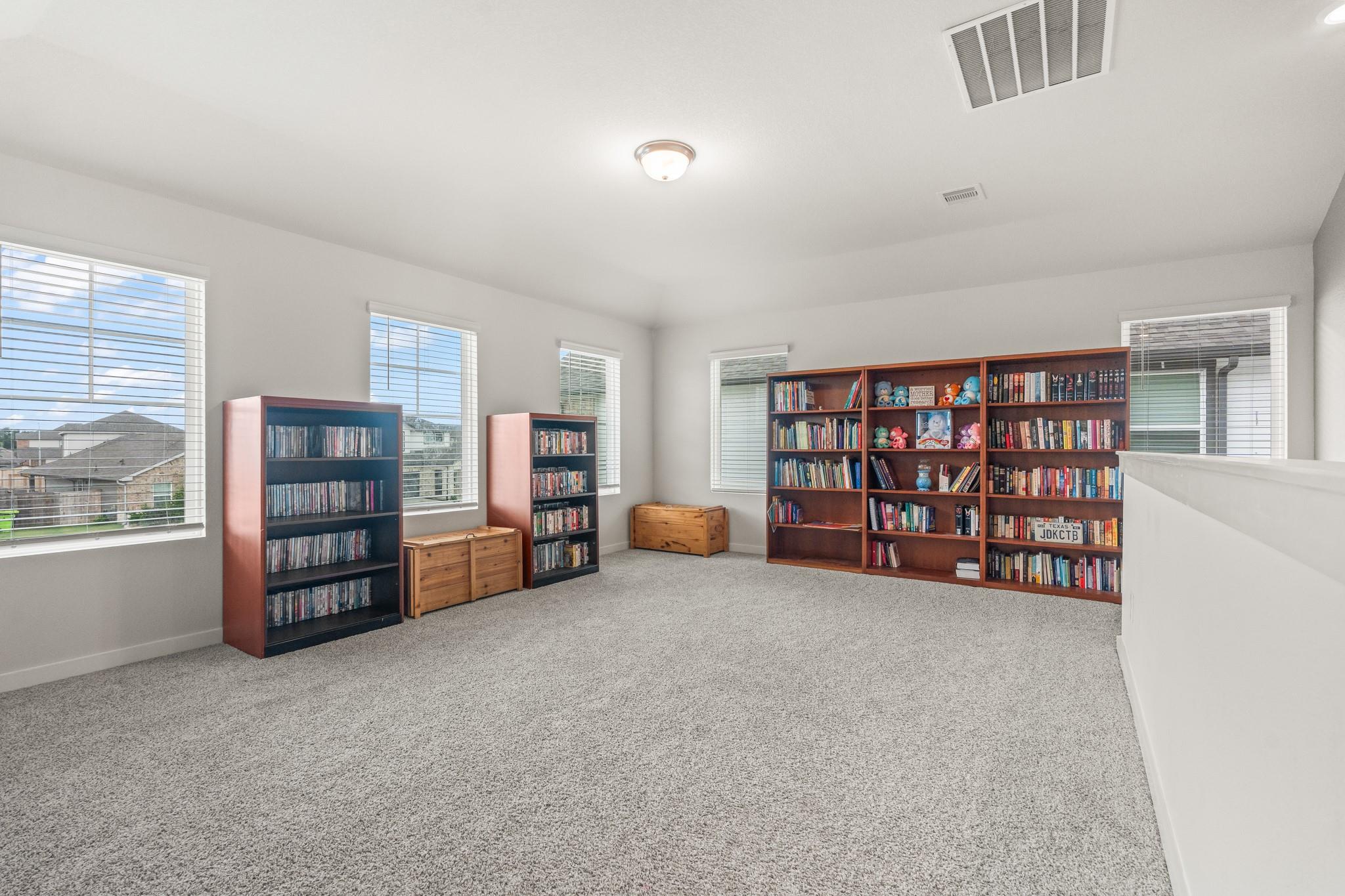 Carpeted upstairs library with book-filled shelves, toy displays, and multiple windows.