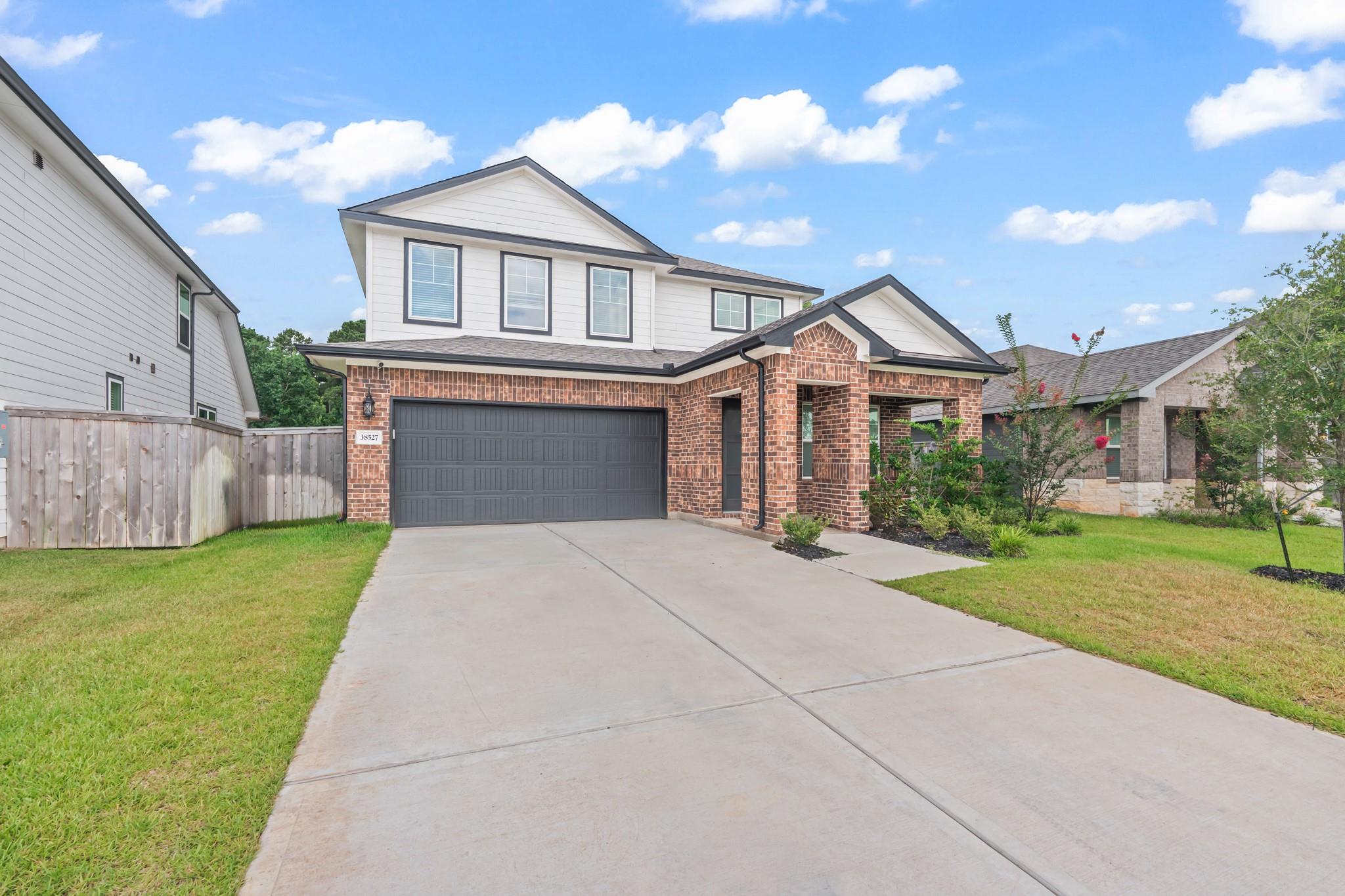 Two-story brick-and-white house with a dark double garage door and wide concrete driveway.