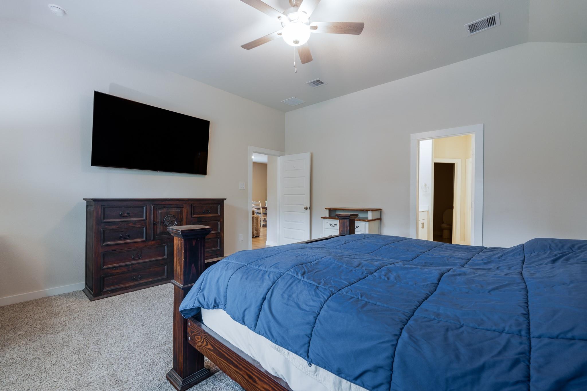 Bedroom with a blue-quilted bed, dark wood dresser, and wall-mounted television.