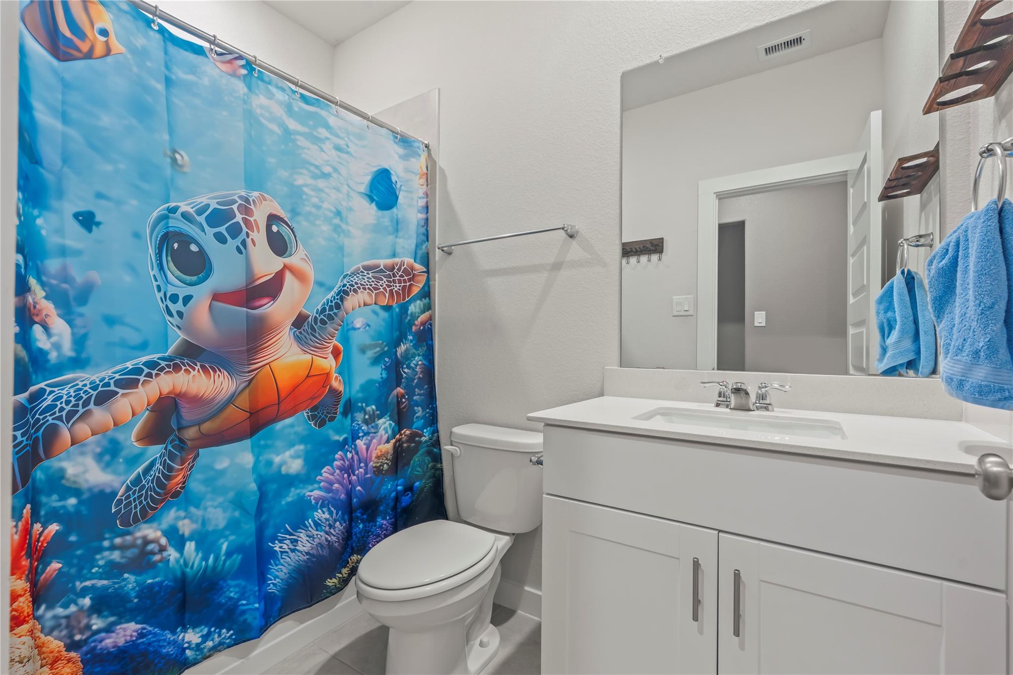 Bathroom with a white vanity and toilet beside a bright blue sea turtle shower curtain.