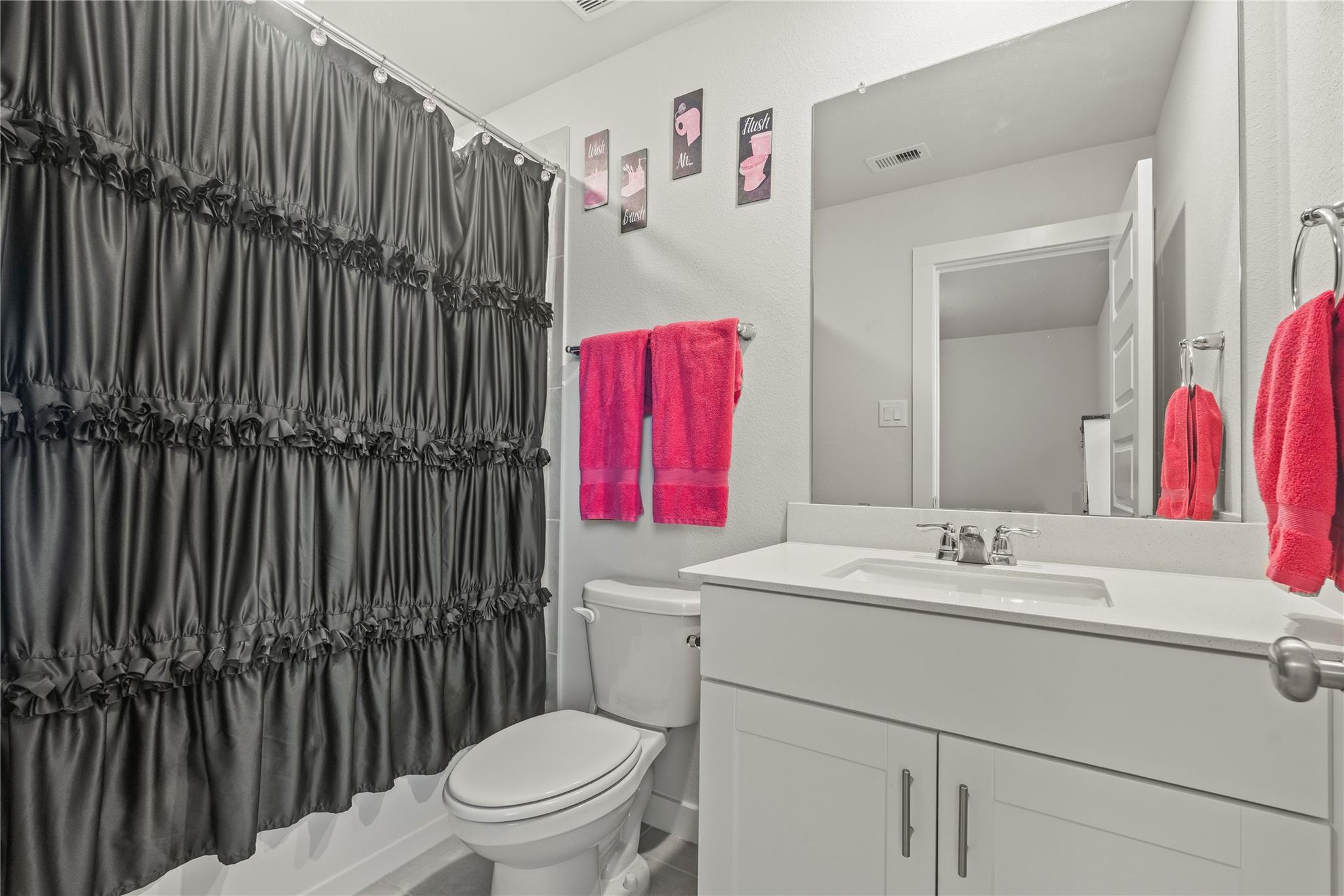 Bathroom with a white vanity and large mirror, dark ruffled shower curtain, and bright pink towels.