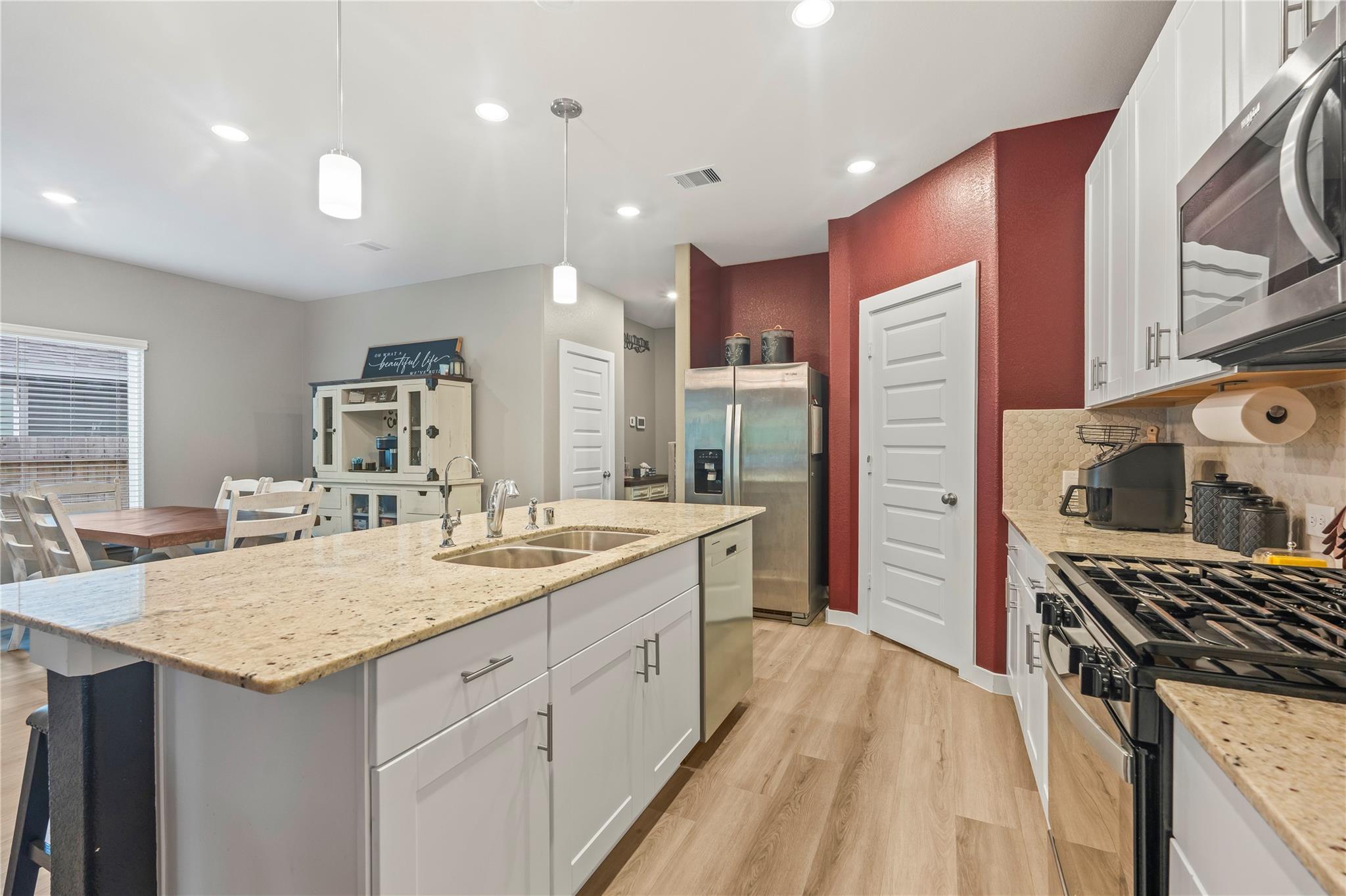 Kitchen with a granite island, white cabinets, stainless appliances, and a red accent wall.
