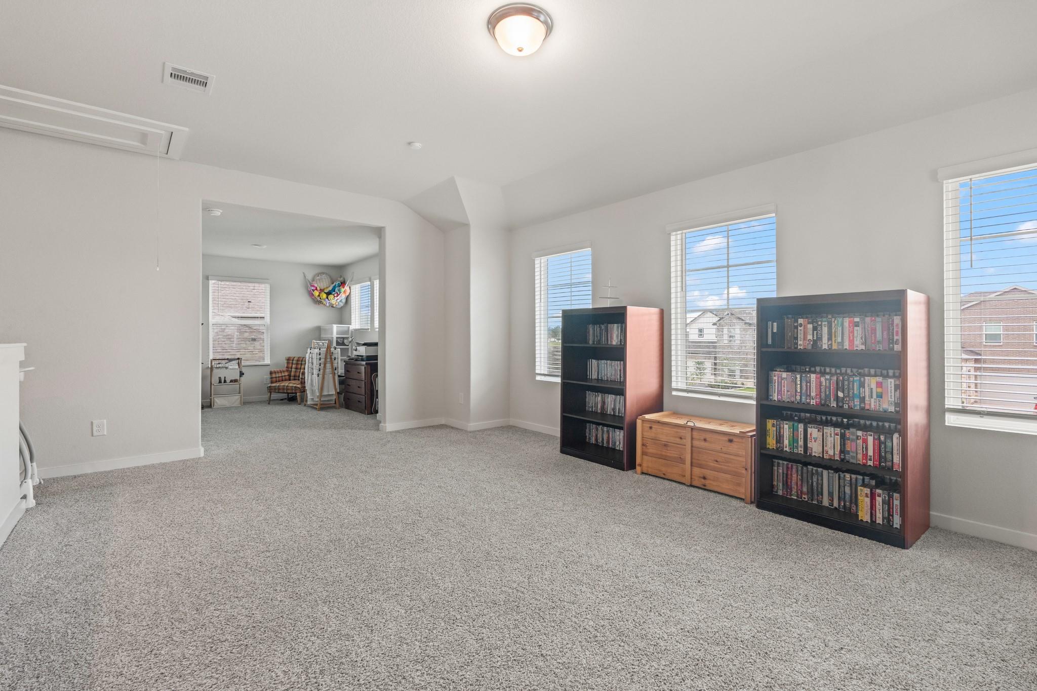 Carpeted bonus room with DVD bookcases, multiple windows, and an adjoining craft nook.