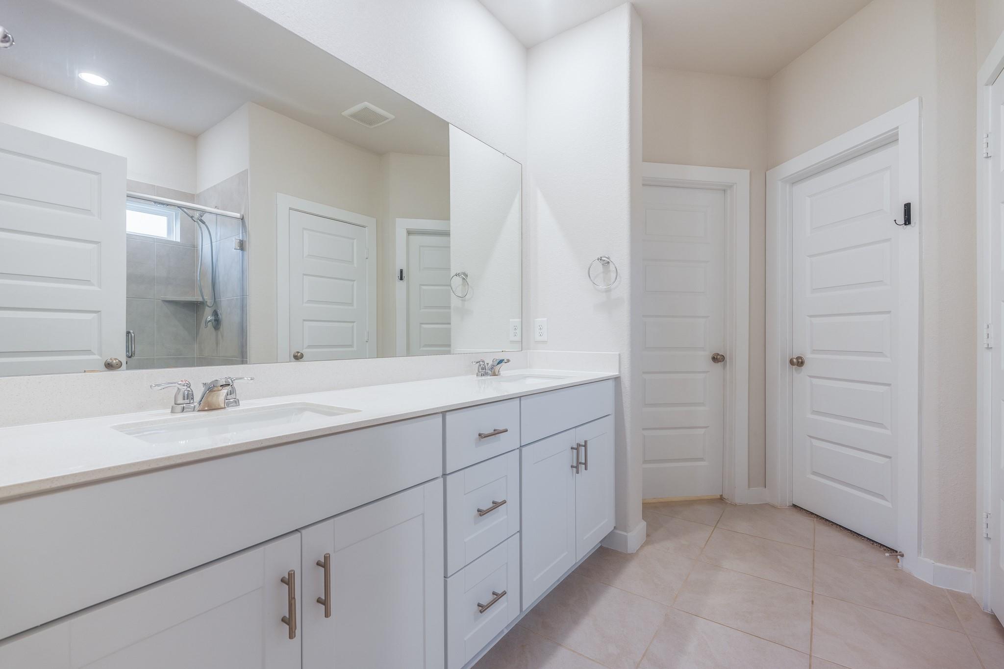 Bathroom with a long white double vanity and glass-enclosed gray-tile shower.