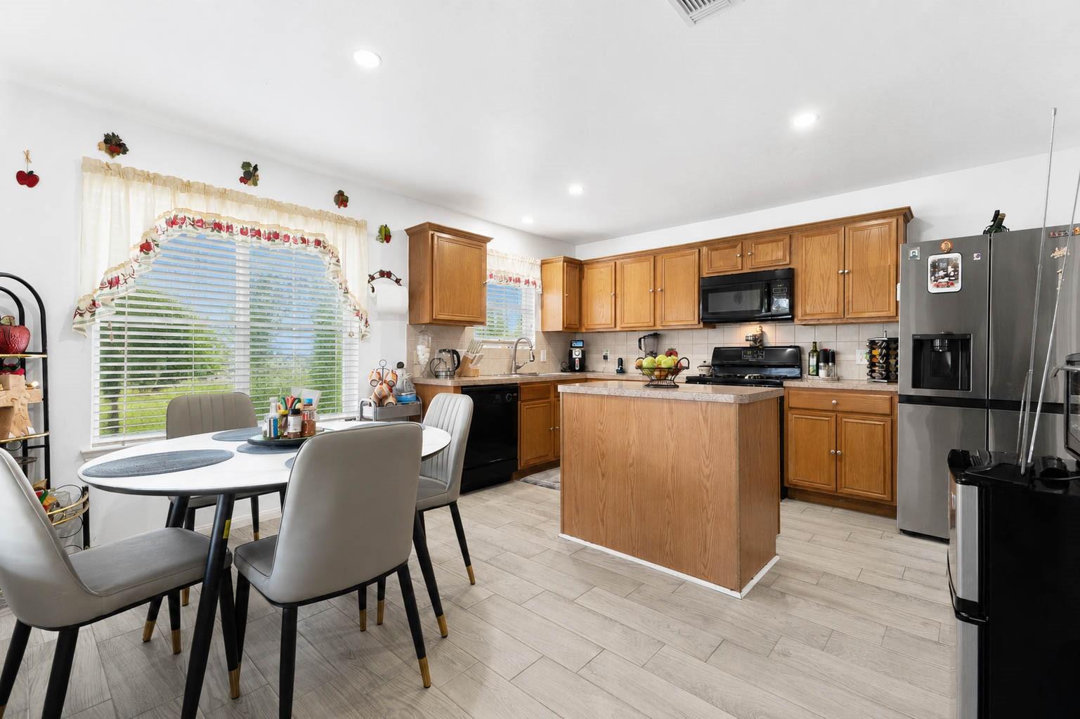 Kitchen with a wood island, honey-colored cabinets, stainless steel appliances, and a window-side dining table.