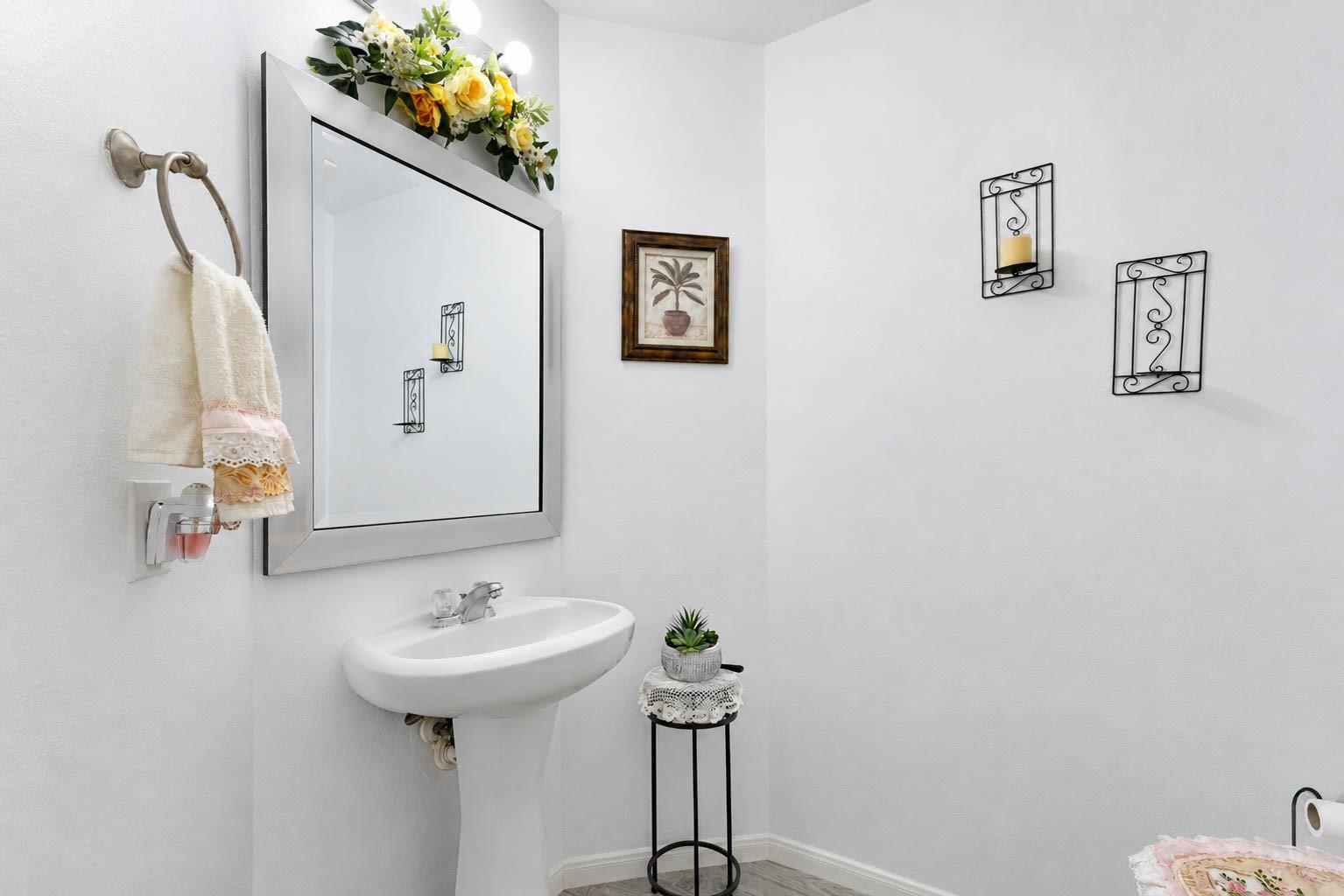 Bathroom with a white pedestal sink, large mirror, and floral decor.