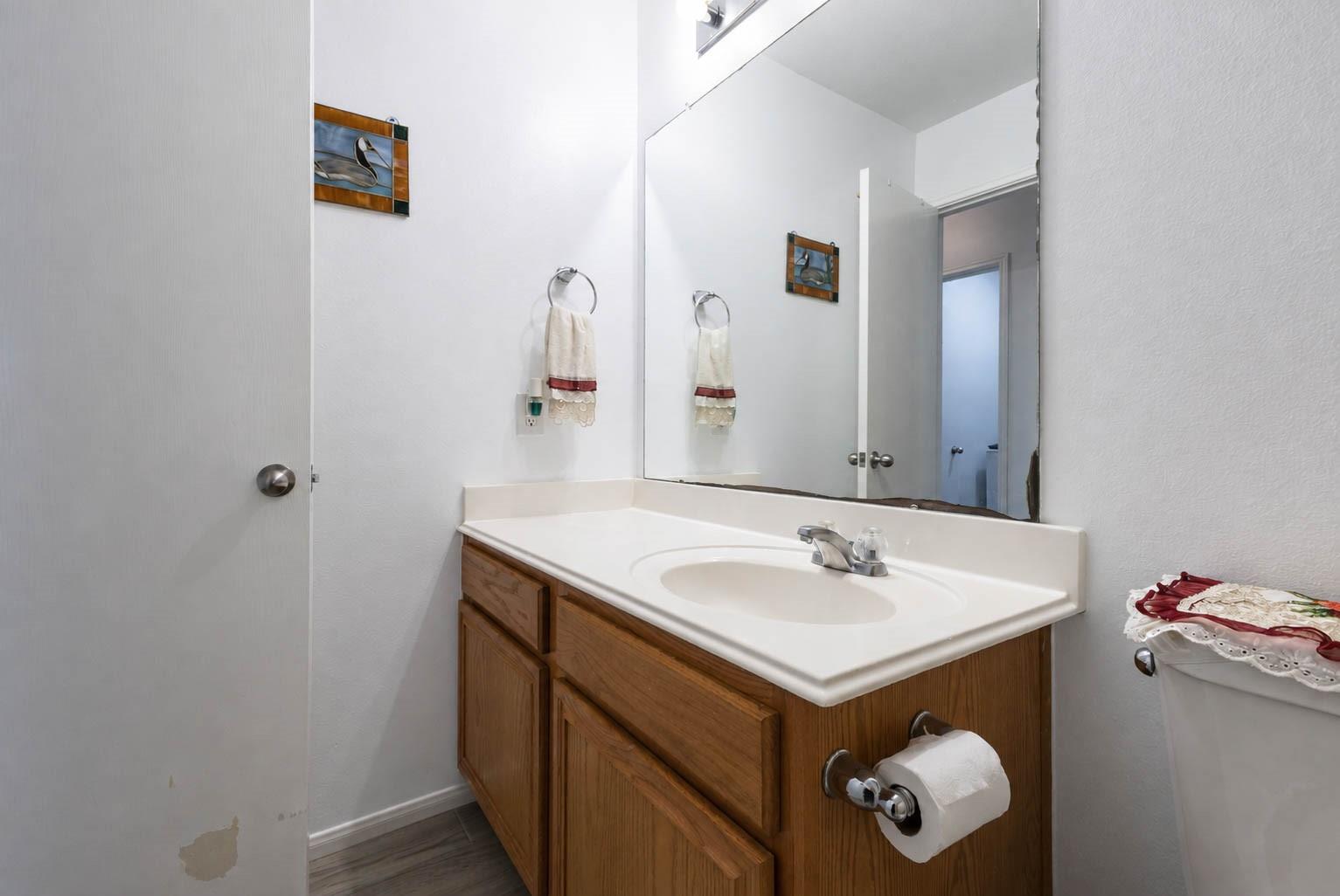 Bathroom vanity with wood cabinets, an oval sink, and a large mirror; peeling paint marks the lower wall.