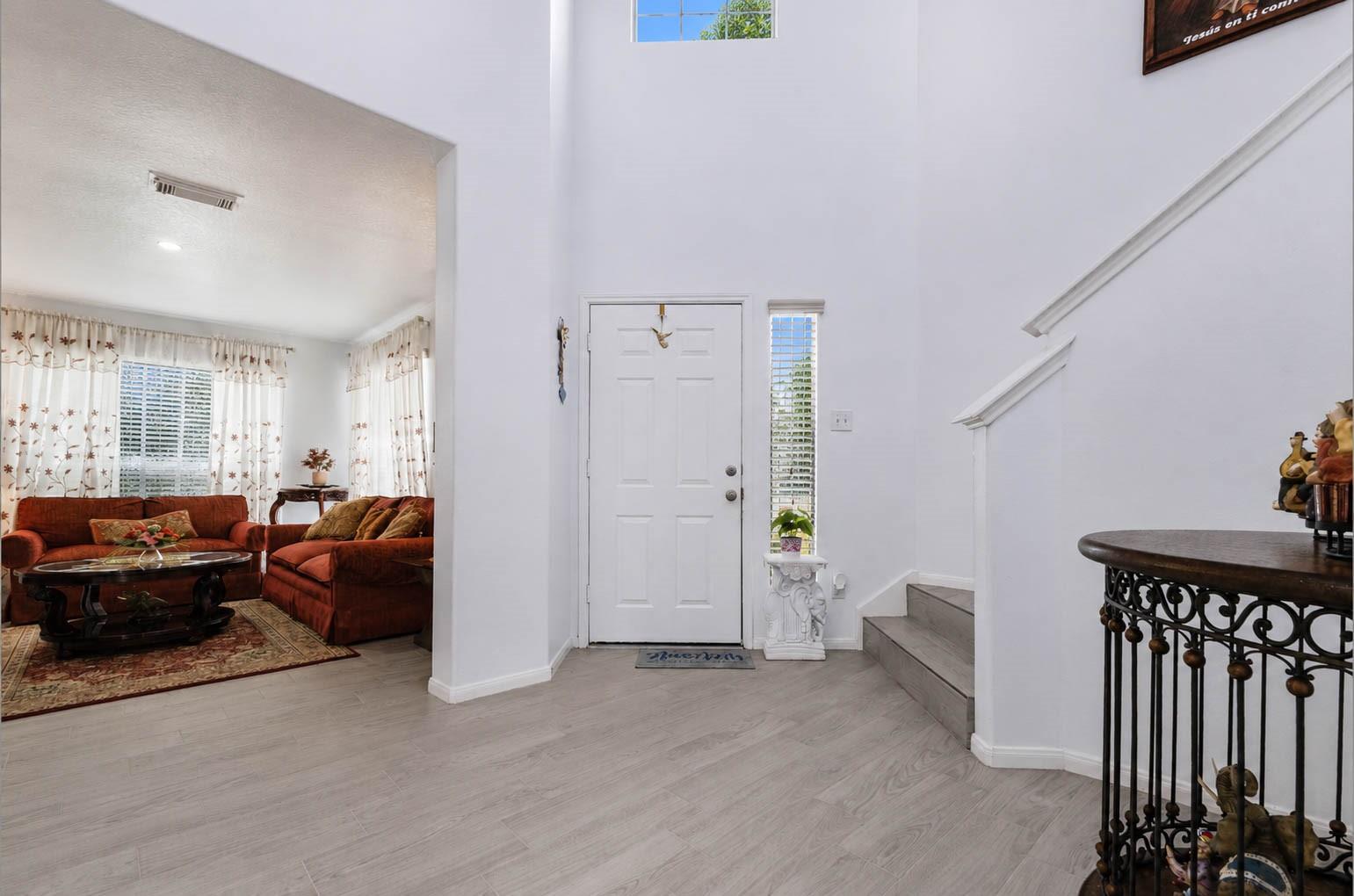 Foyer with a white front door and staircase opening onto a living room with rust-colored sofas.