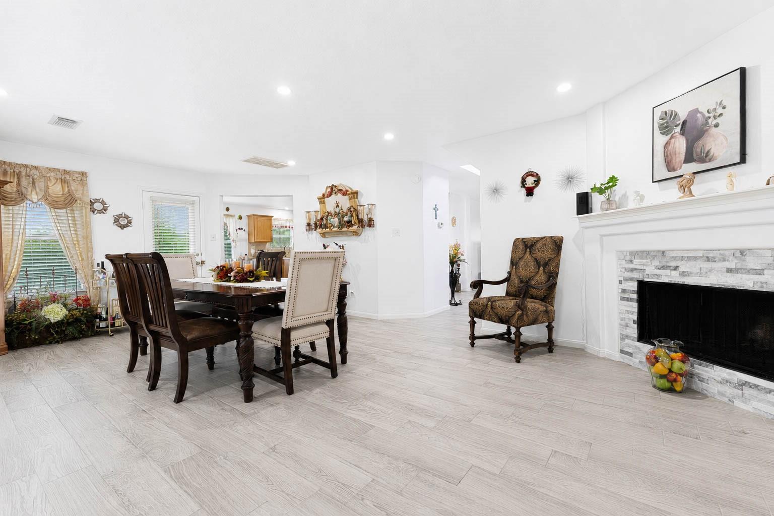 Dining and living area with a dark wood table, light tile floors, and a stone-surround fireplace.
