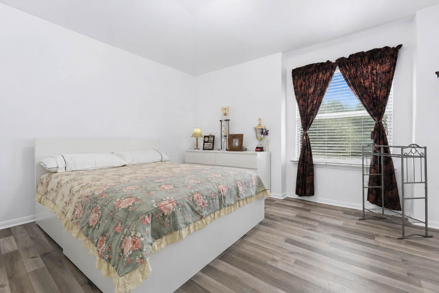Bedroom with a large floral-quilted bed, dark curtains, and gray wood-look flooring.